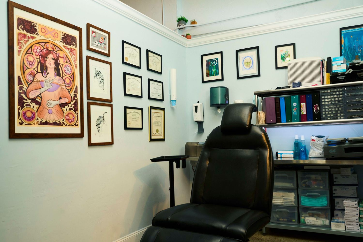 Professional tattoo studio room with black chair, framed artwork, and organized supply shelves.