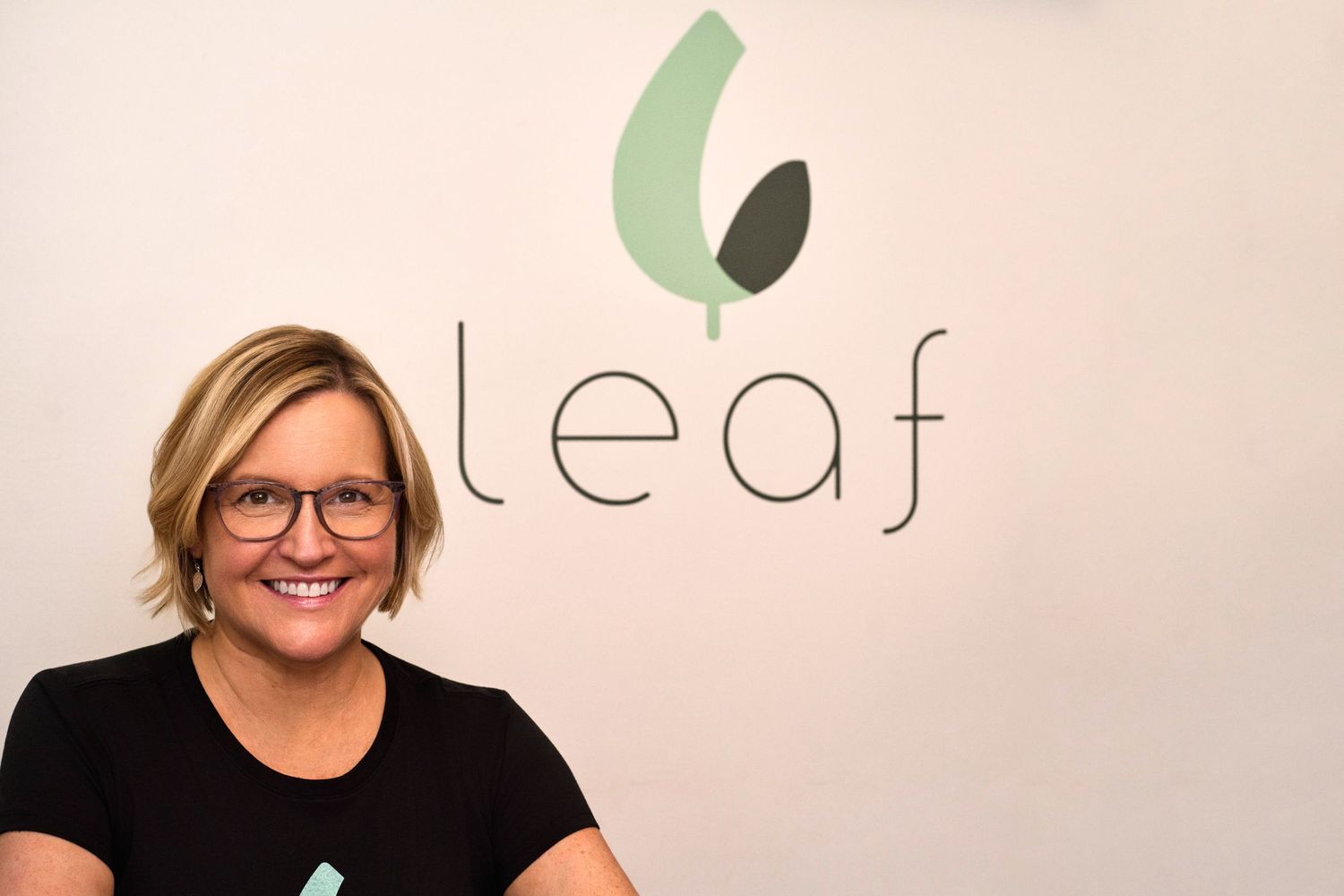 Smiling woman in black t-shirt posing in front of the Leaf brand logo.