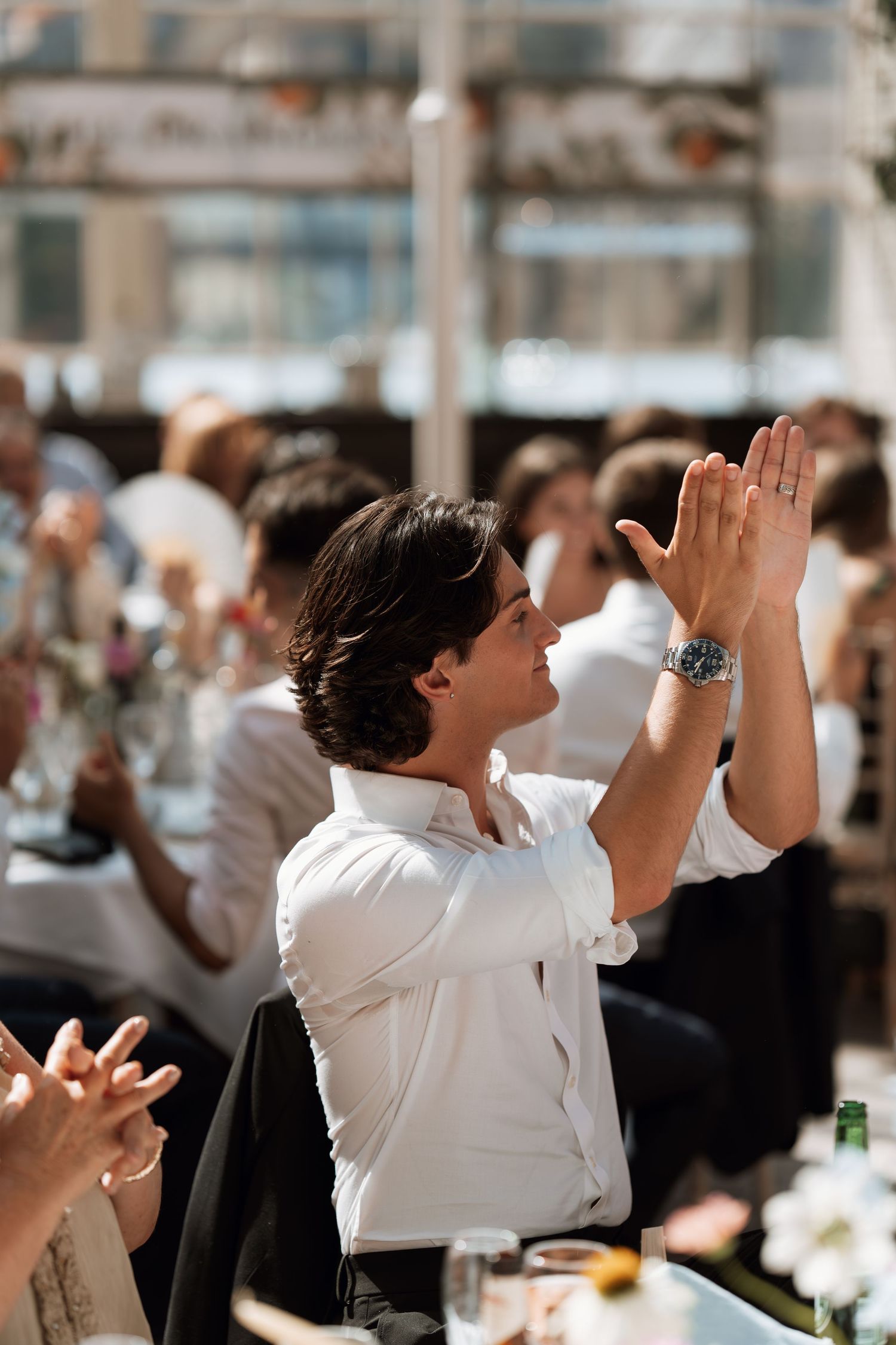 Person in white dress shirt enthusiastically cheering and raising their hands during a crowded indoor event.