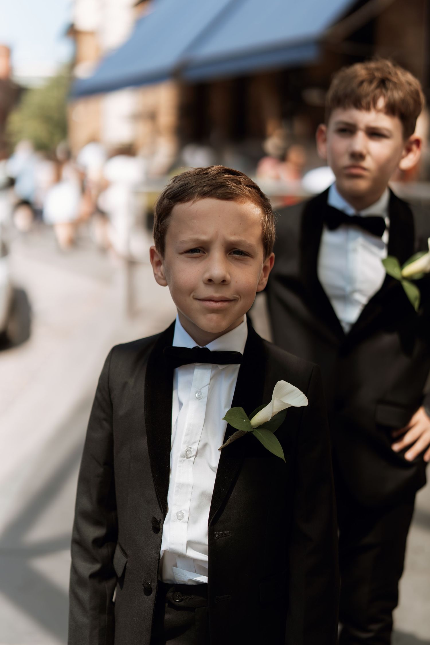 Young attendants in black tuxedos with white boutonnieres at a formal event.