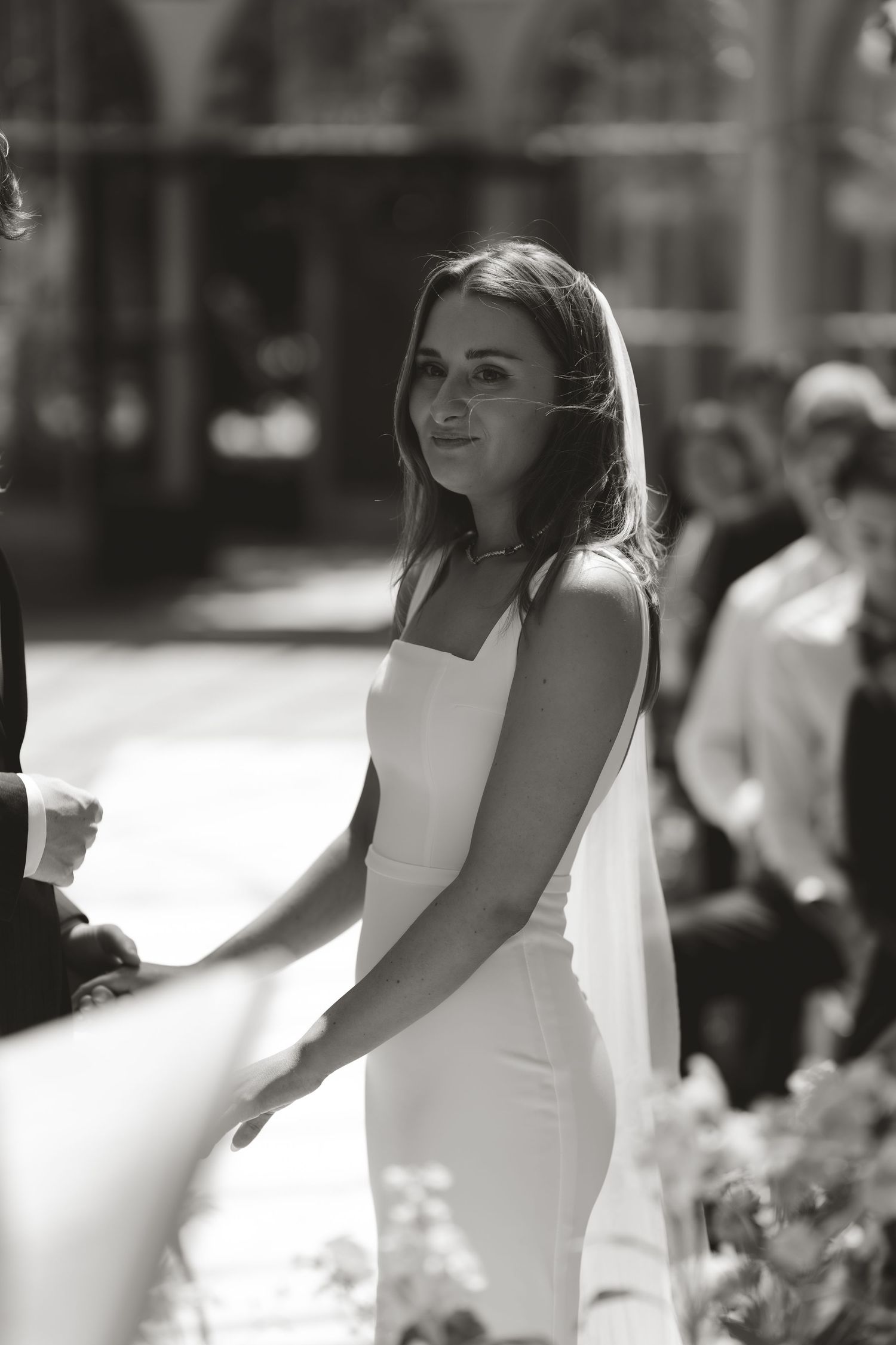 Elegant black and white portrait of smiling bride in a sleek white dress with natural lighting outdoors.