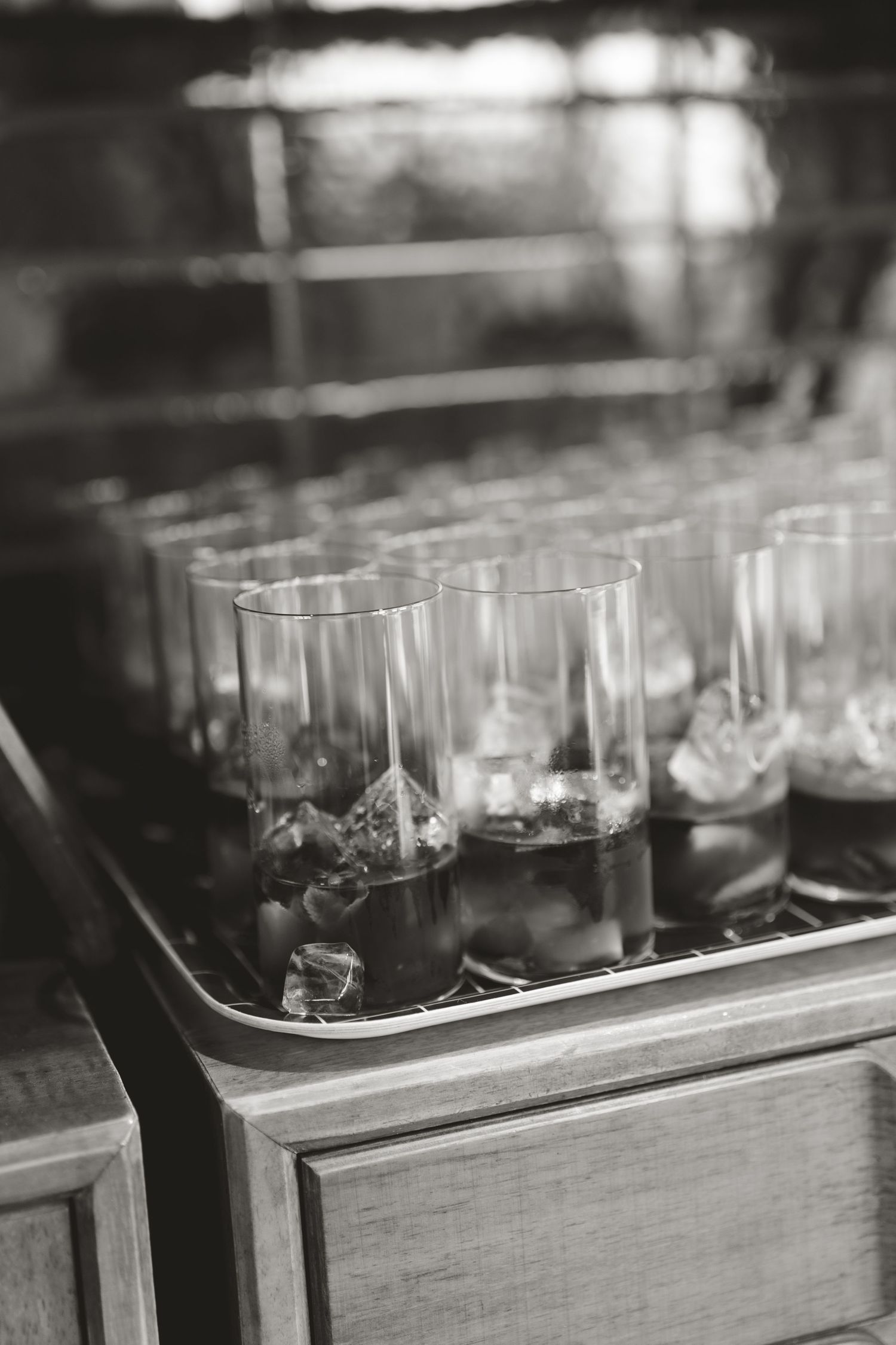 Black and white photo of cocktail glasses arranged in rows on a wooden bar cart.