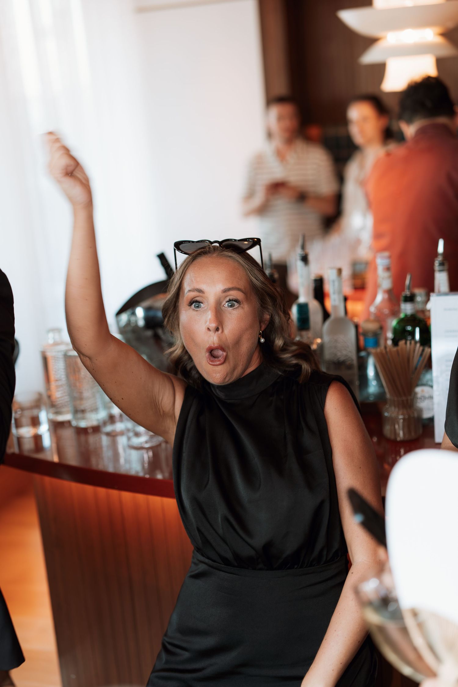 Party guest in black dress dancing enthusiastically at reception bar.
