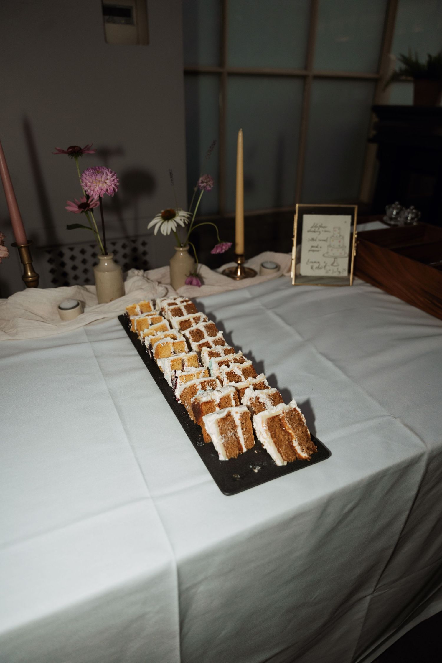 A display of artistically arranged dessert bites on a white tablecloth with candlelight and flowers.