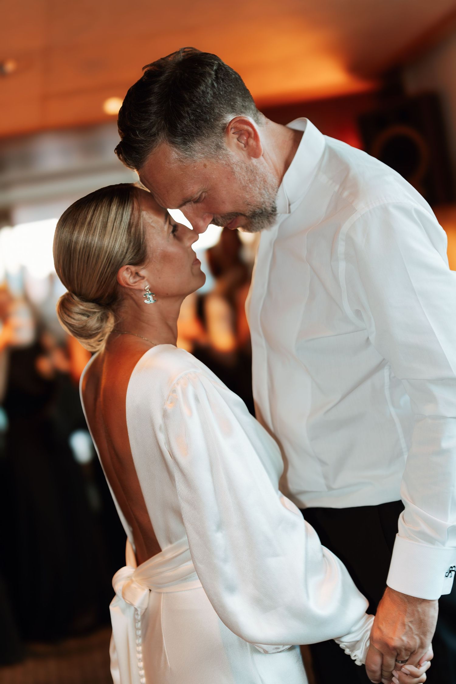 A romantic moment between a couple in elegant white attire sharing an intimate moment at what appears to be their wedding.