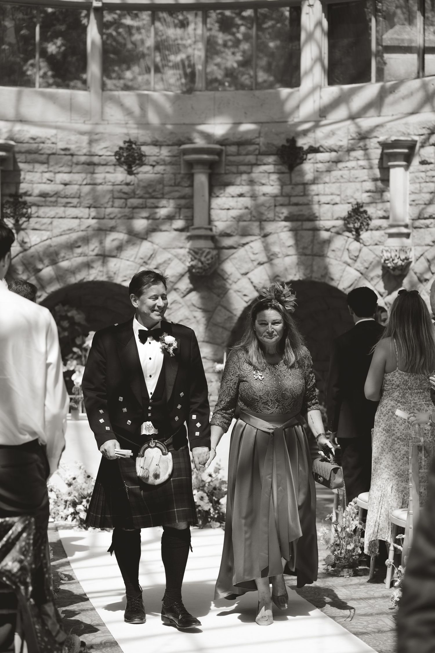 Wedding couple walks together after ceremony, groom wearing traditional Scottish kilt and formal attire at outdoor venue.