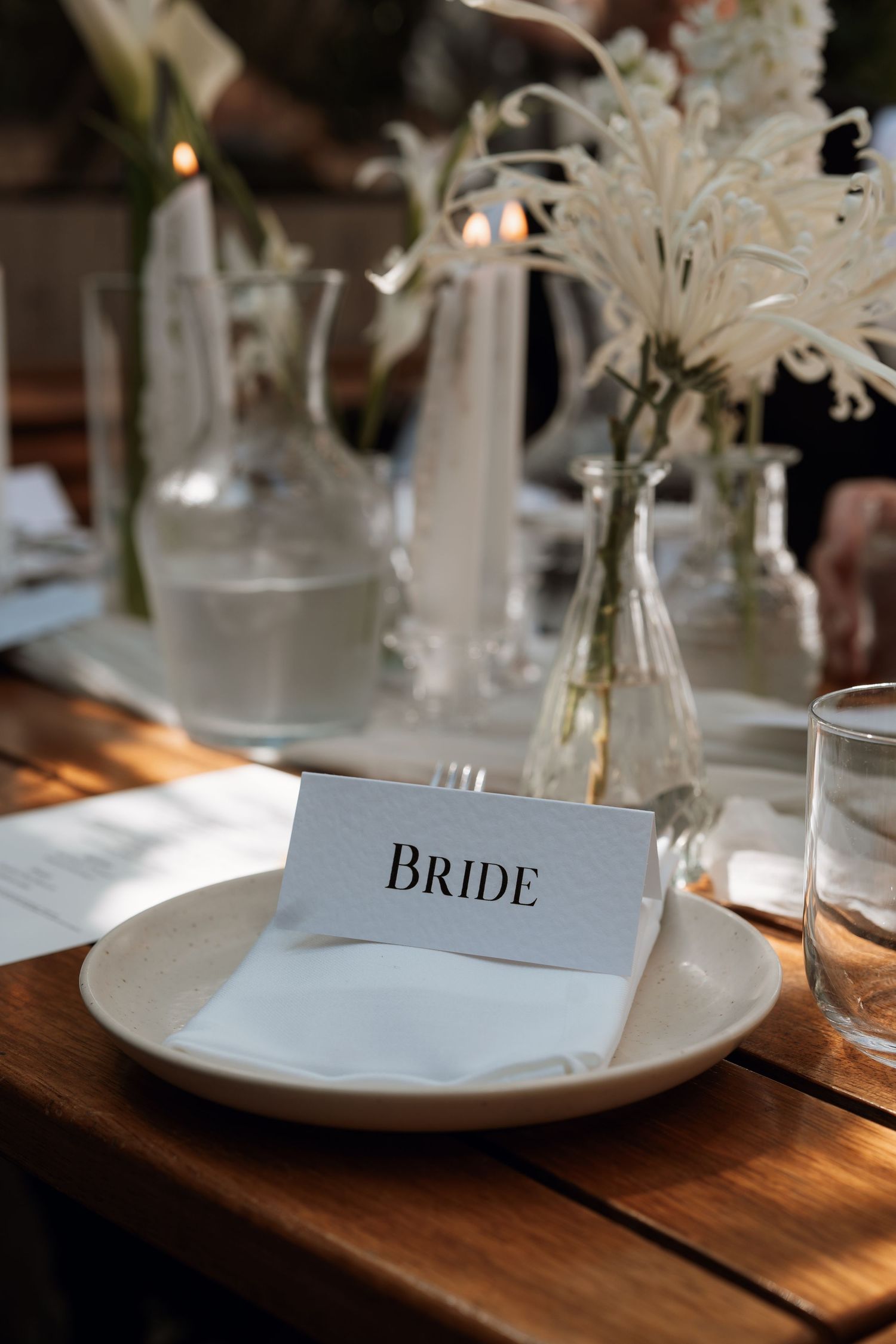 Elegant wedding place setting with name card labeled 'BRIDE' on white plate and rustic wooden table setting.