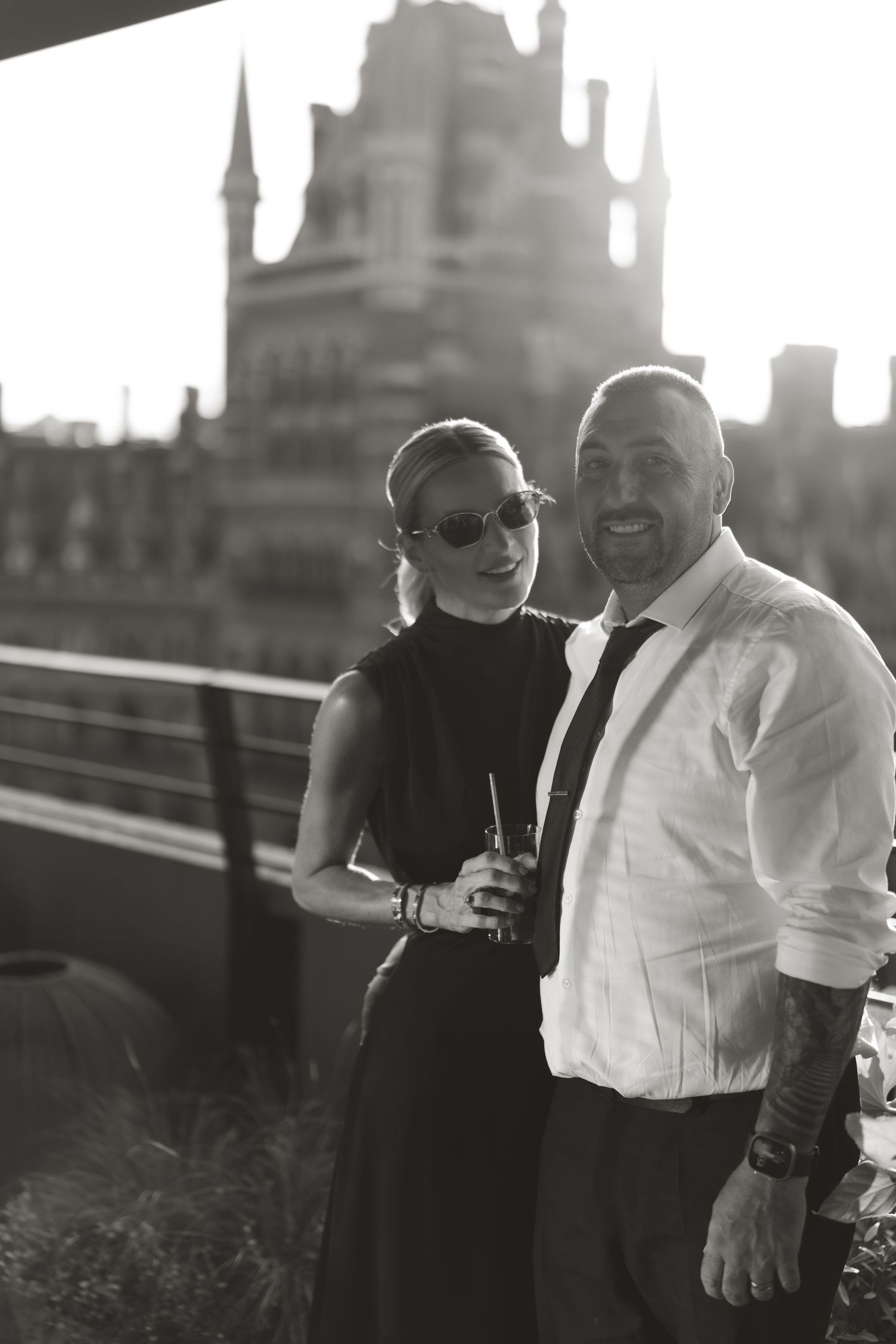 Couple in black and white attire sharing intimate moment on rooftop with city skyline in background.