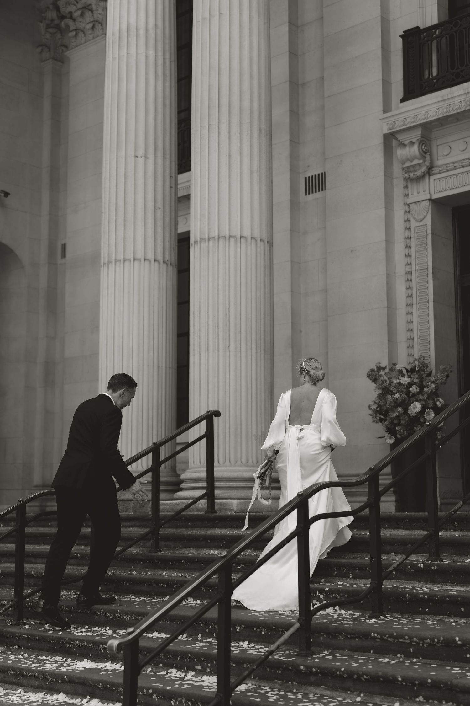 Black and white wedding photo sequence showing a couple walking down stairs beside classical columns.