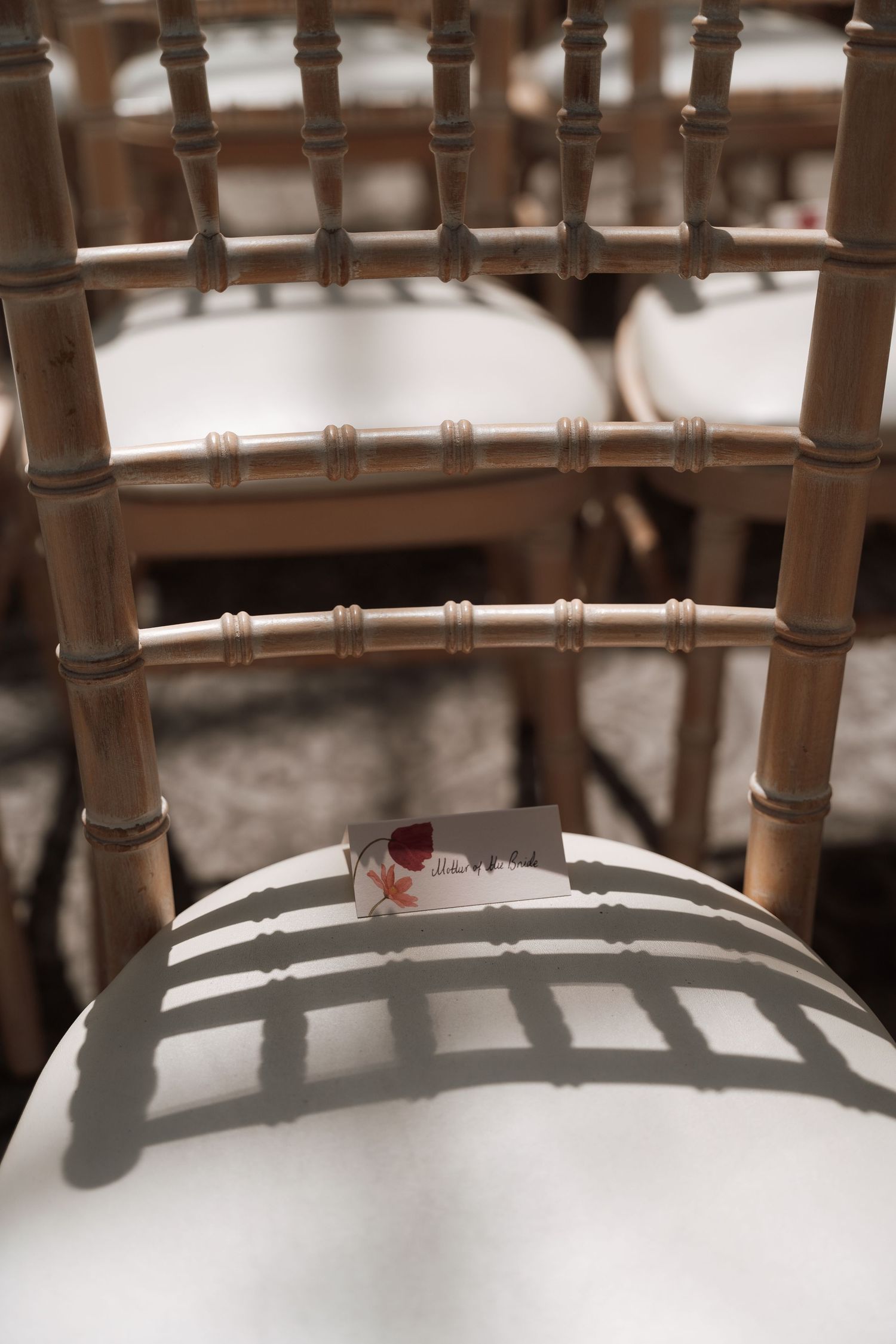 Wooden bamboo-style chair with shadows casting striped patterns on a white cushioned seat.