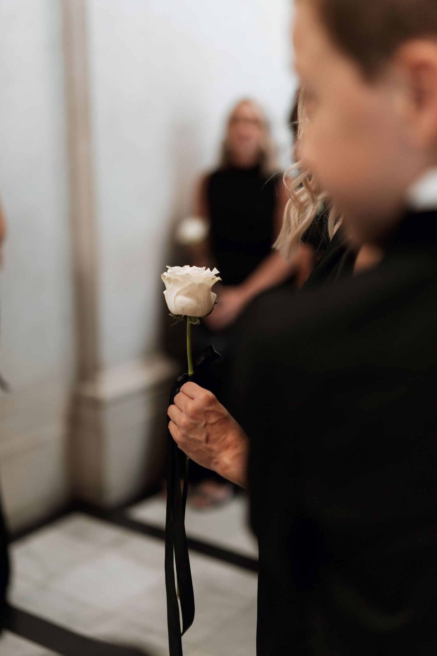 A single white rose being held at a formal event with a blurred background.