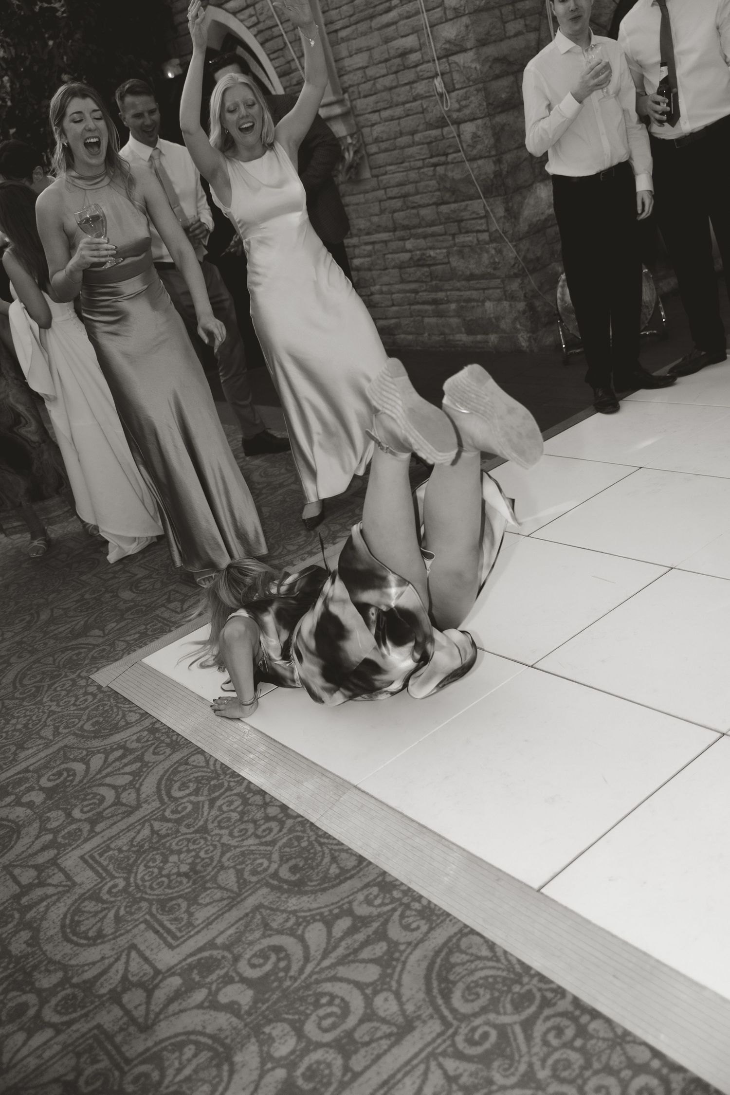Black and white photo of wedding guests dancing and having fun on a checkered dance floor.