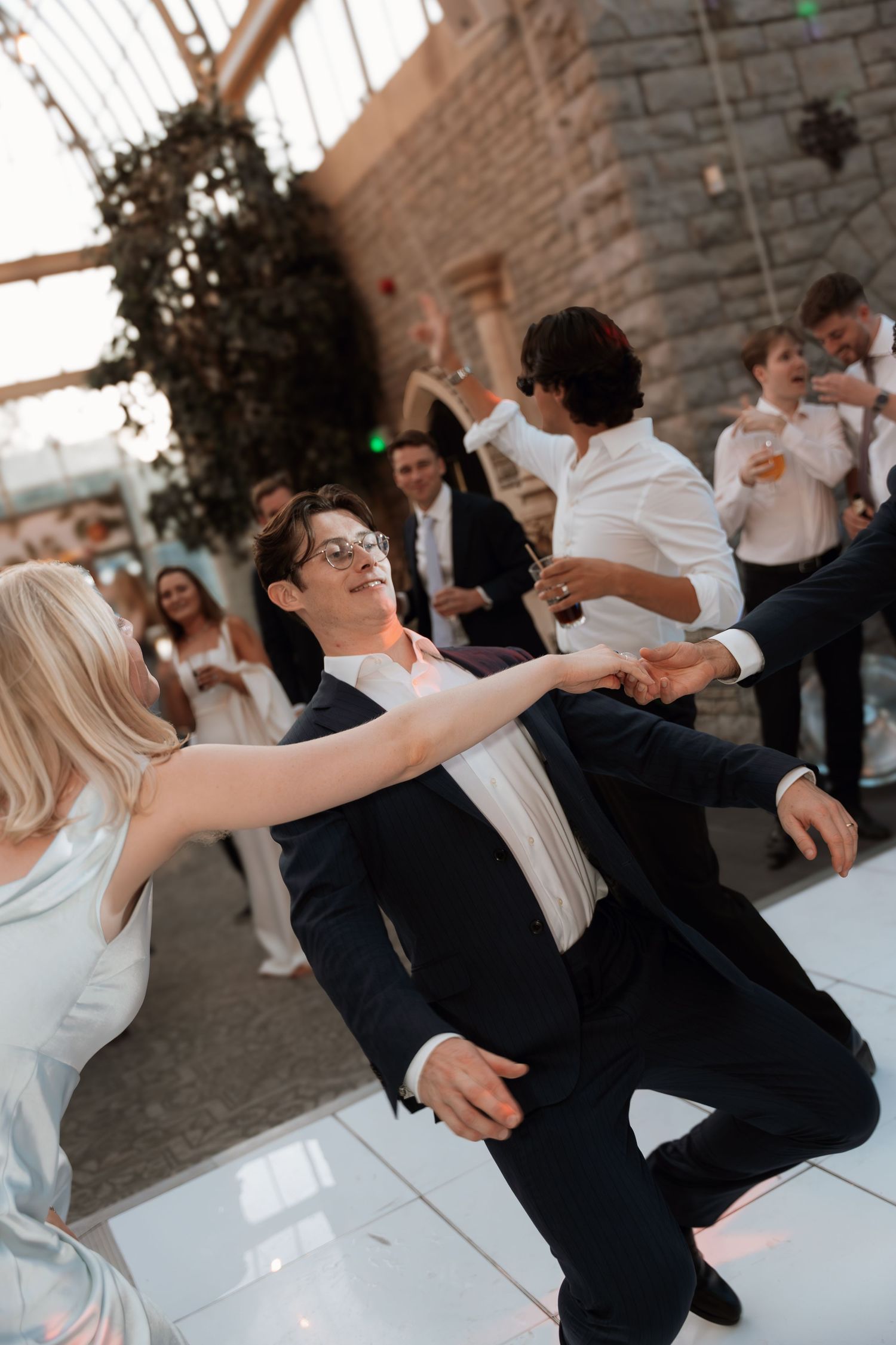 Wedding guests dancing exuberantly on a white dance floor at the reception.