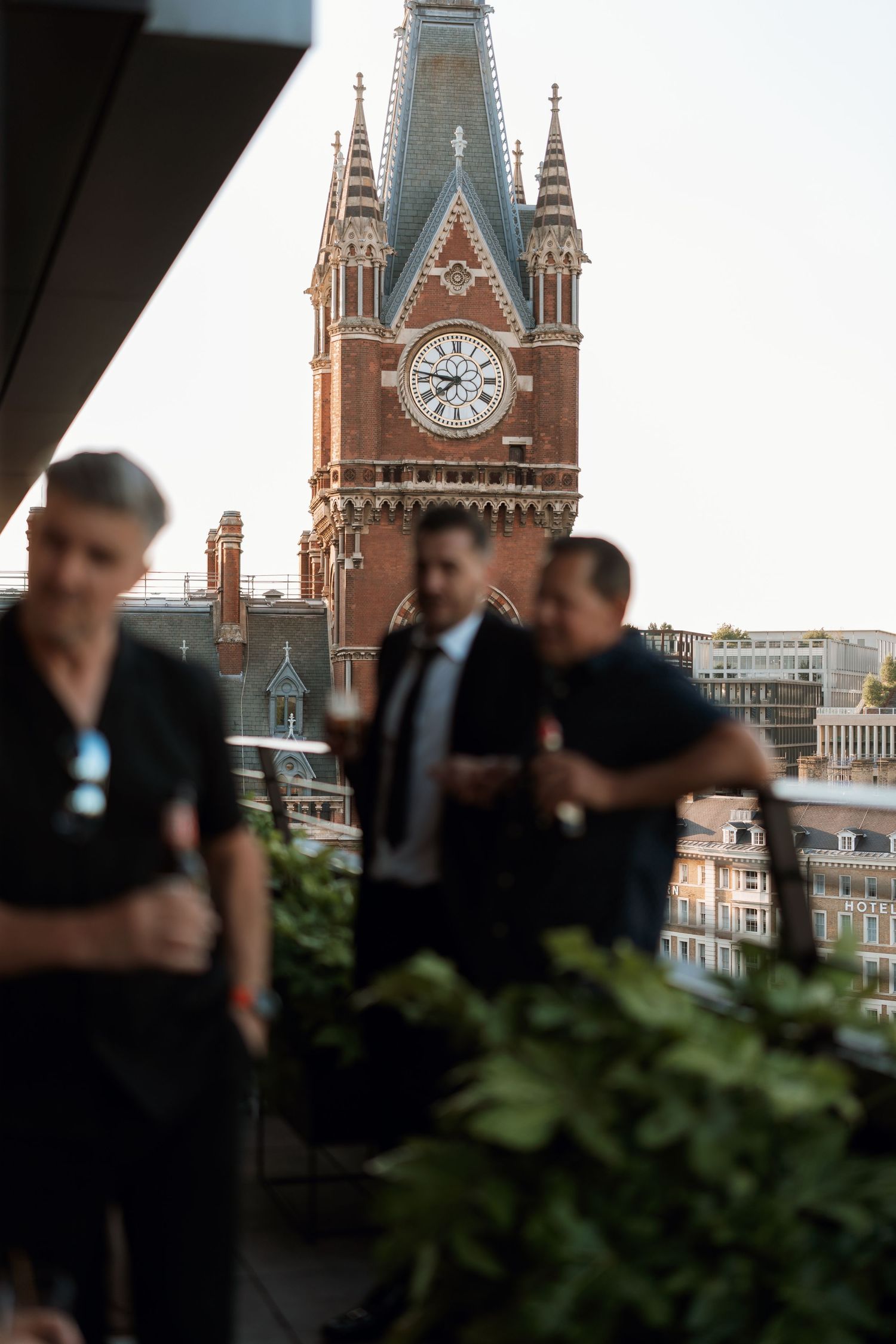Gothic church tower with clock face visible as people gather on a rooftop terrace.