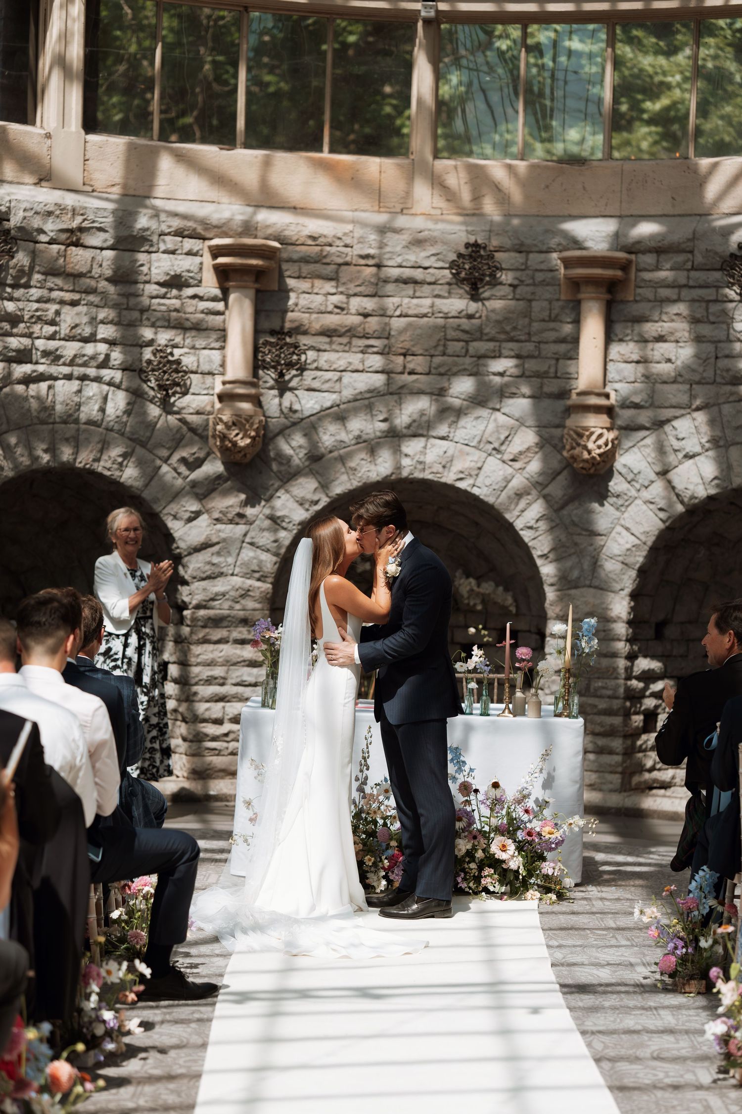 A sequence of wedding photos showing a romantic first kiss against a stone archway and floral backdrop.