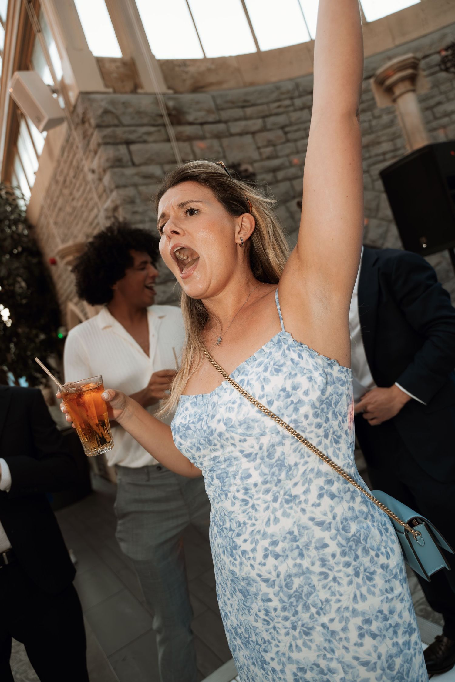 A wedding guest in a blue floral dress dances energetically at the reception.