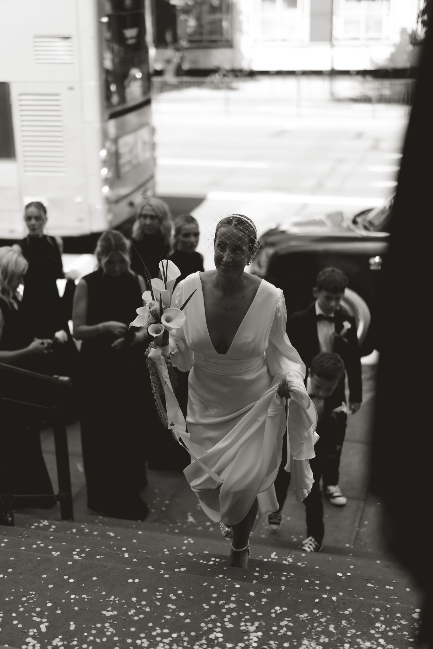 A black and white photo of someone descending stairs in an elegant white dress at an event.