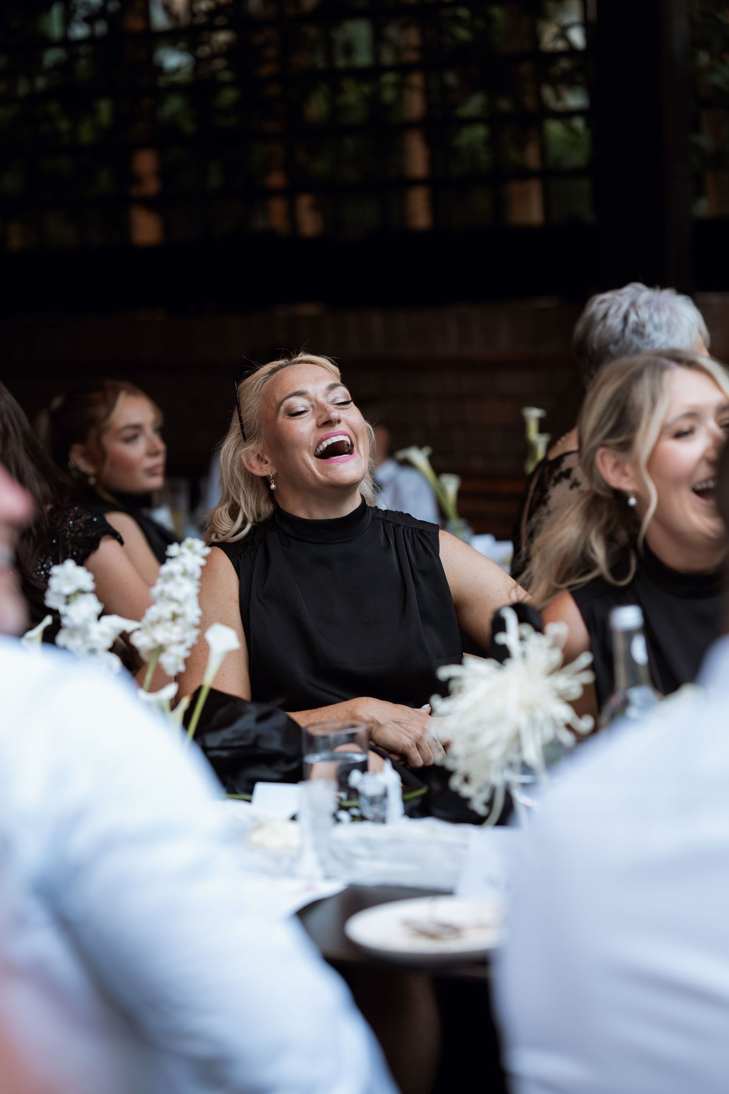 A group of wedding guests share joyful laughter during an outdoor reception celebration.