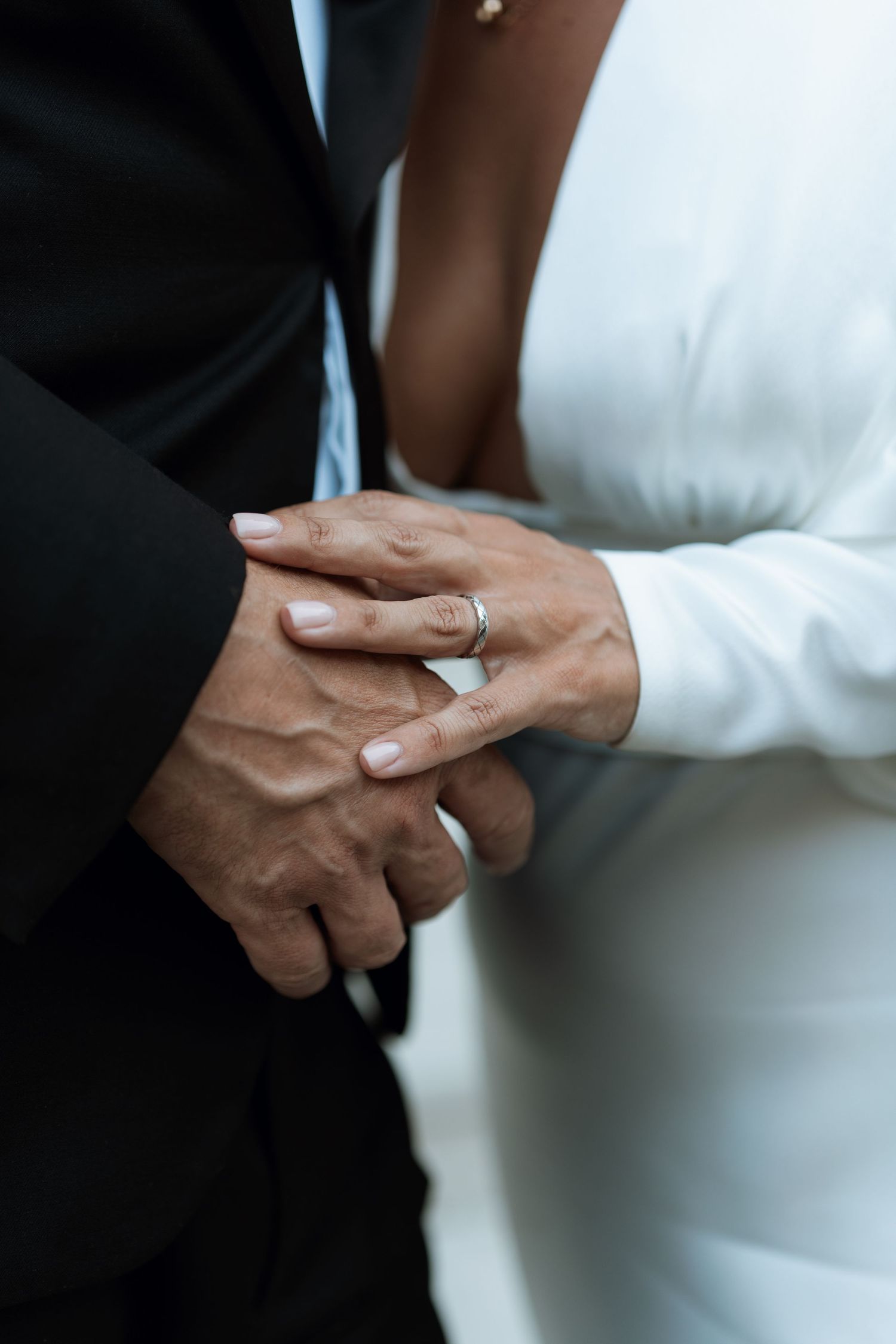 Close-up detail shots of hands exchanging wedding rings during a ceremony against a black and white background.