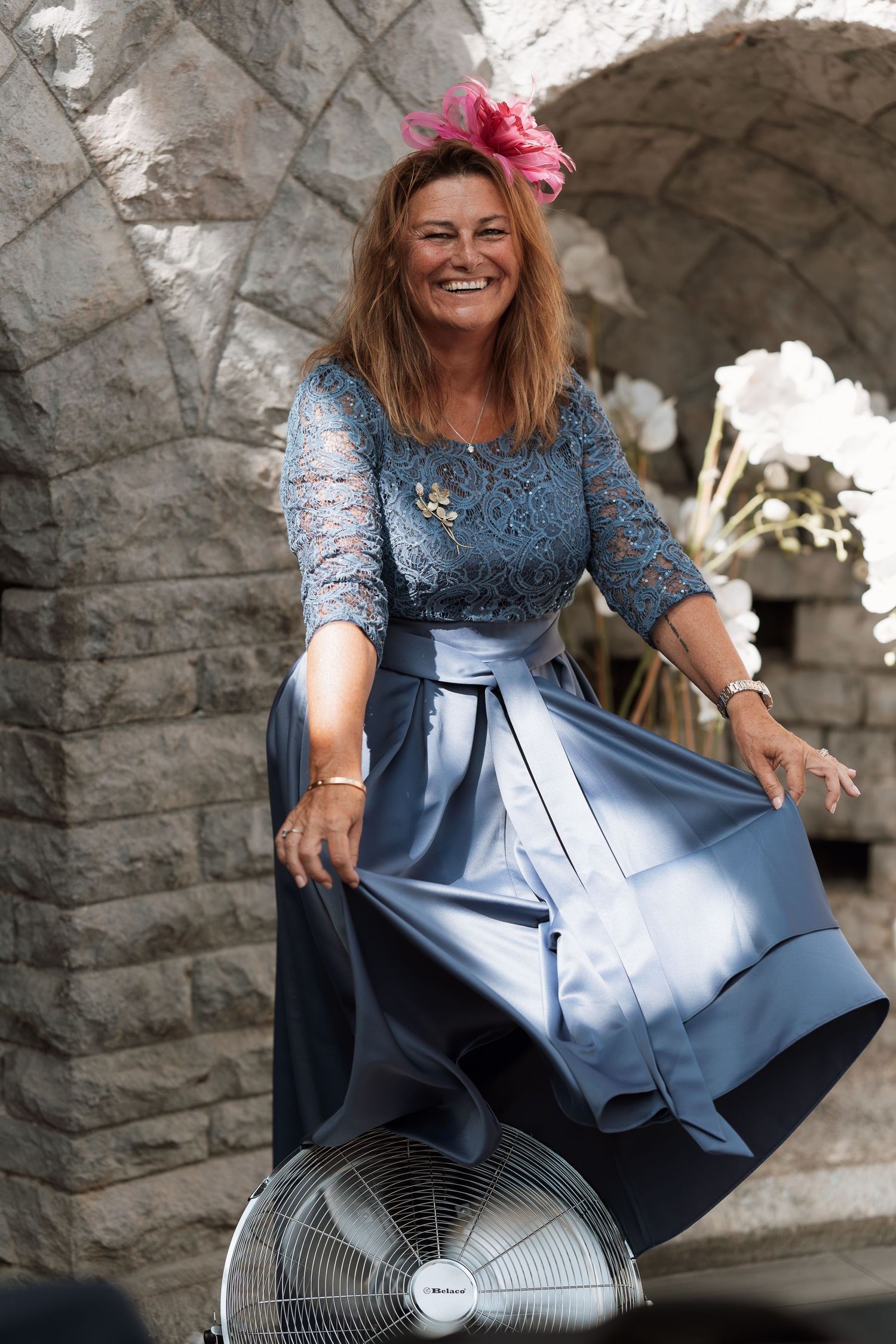 Person in a blue lace dress playfully twirling their skirt against a stone wall background.