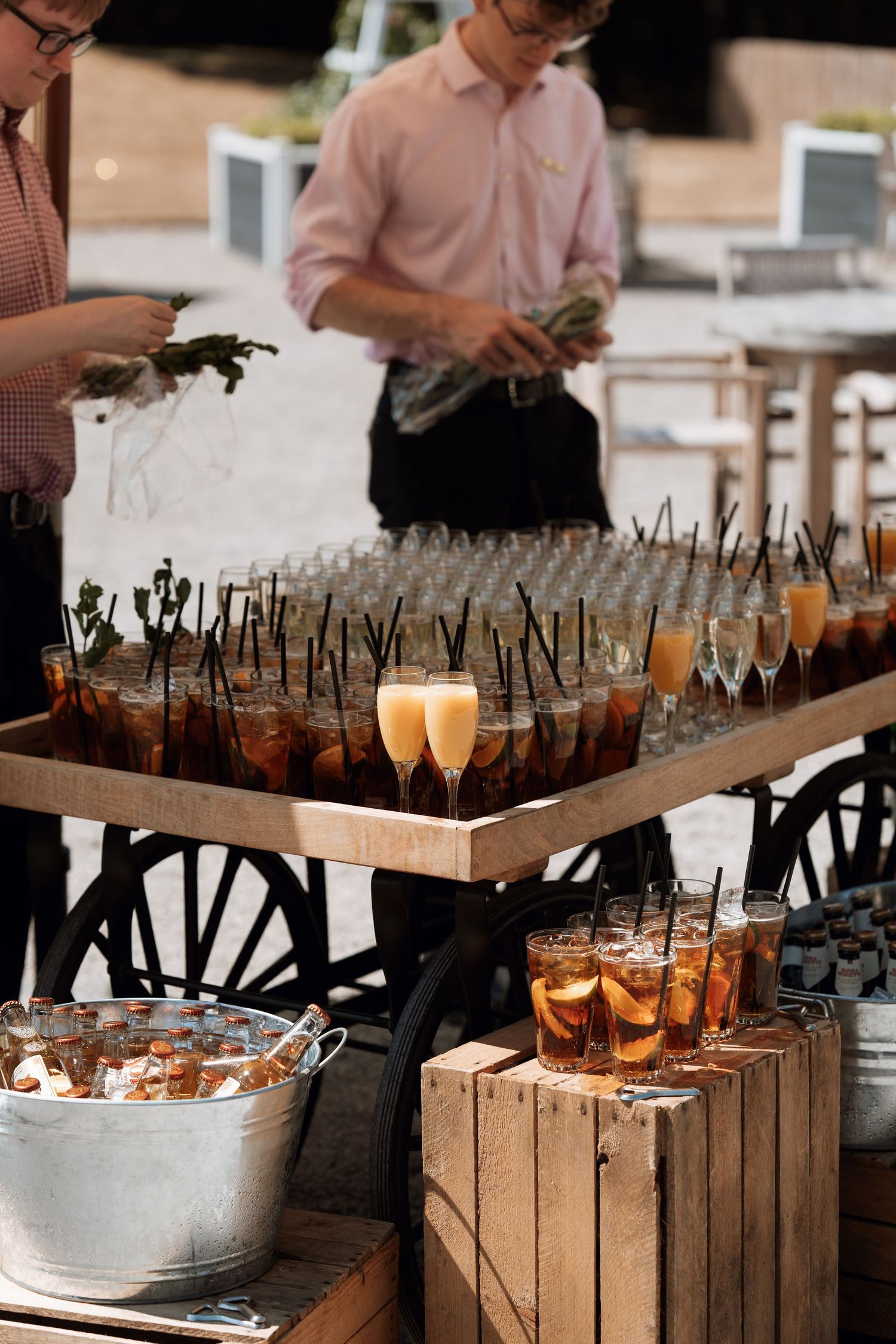 Various cocktails and champagne glasses arranged on wooden serving trays at an upscale event bar setup.