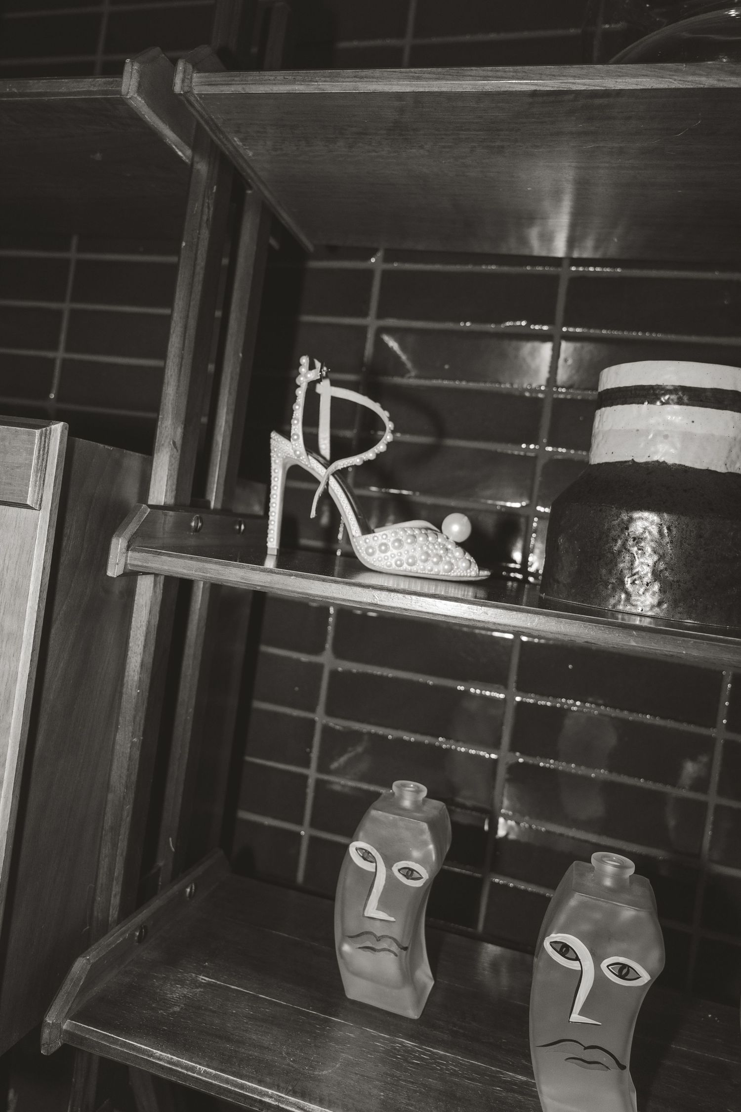 A black and white photograph shows storage shelves with a bicycle part and glass containers decorated with face designs.