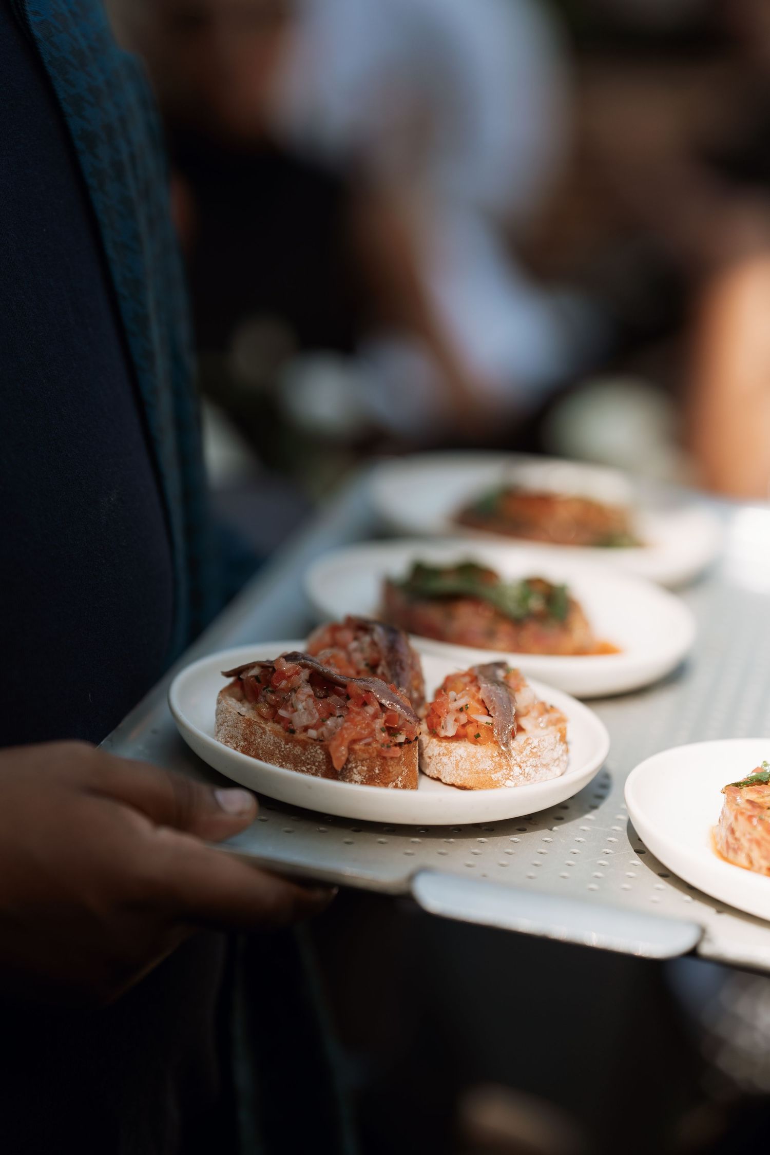 Multiple shots of plated food being served on white dishes in dimly lit setting.