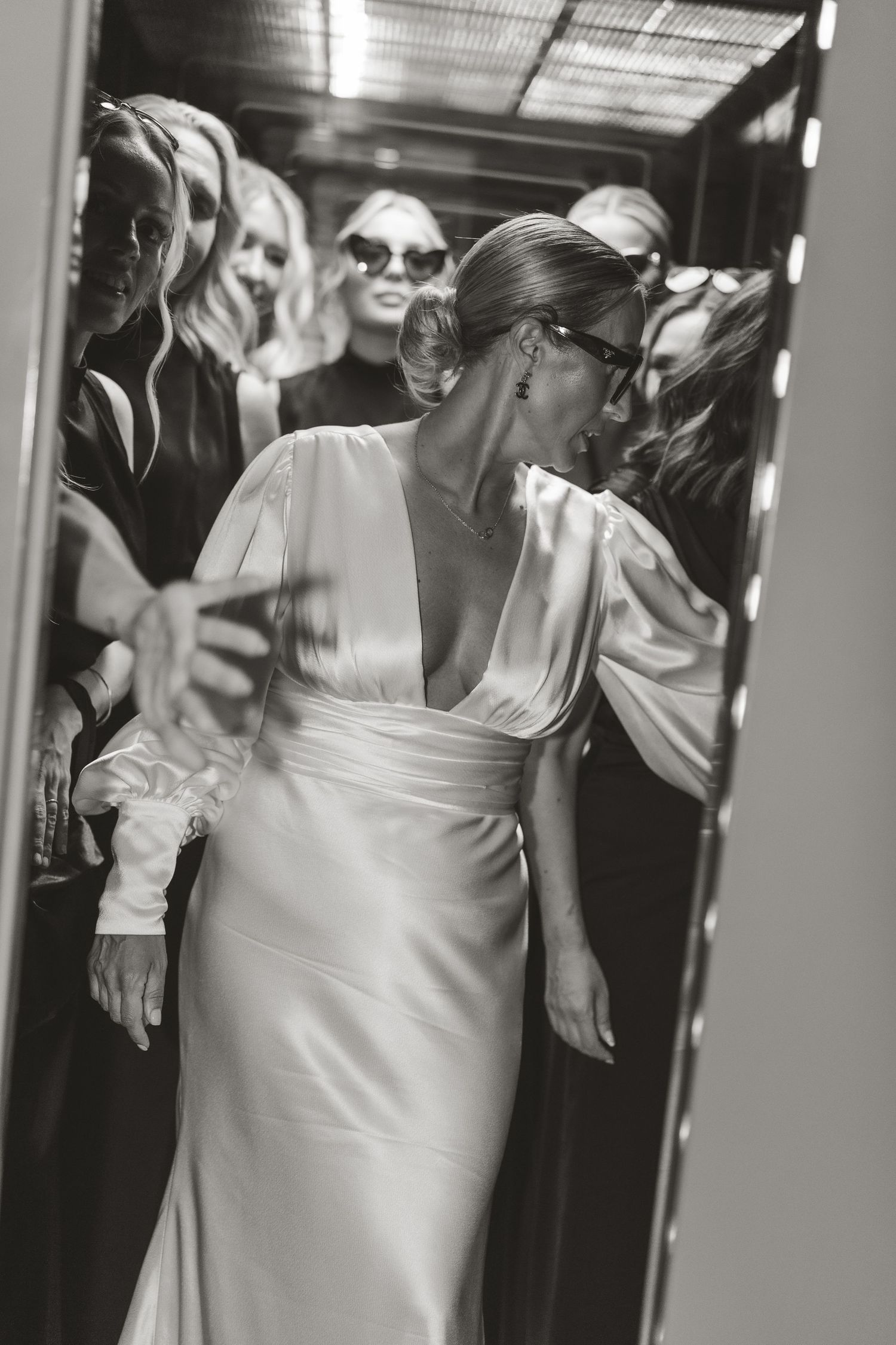 Black and white photo of a bride in an elegant white dress with statement sleeves in an elevator with guests.