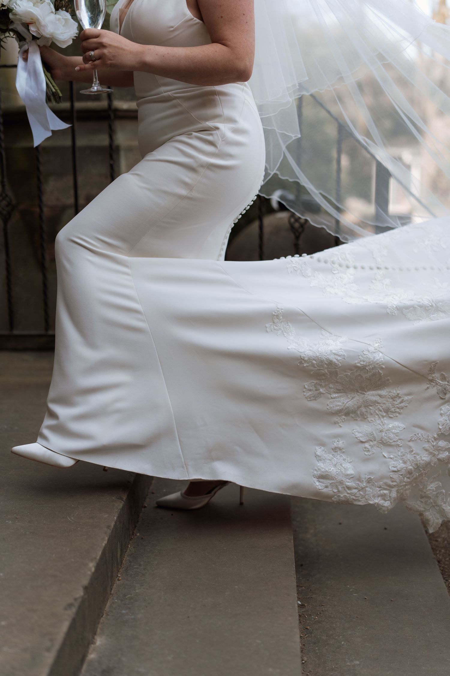 A white wedding dress with intricate lace detailing flows elegantly across stone steps.