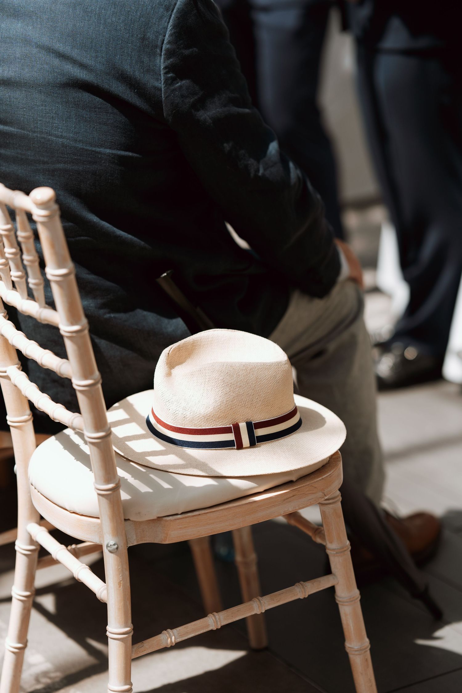 A row of white sun hats resting on wooden chair backs in a shadow-lit setting.