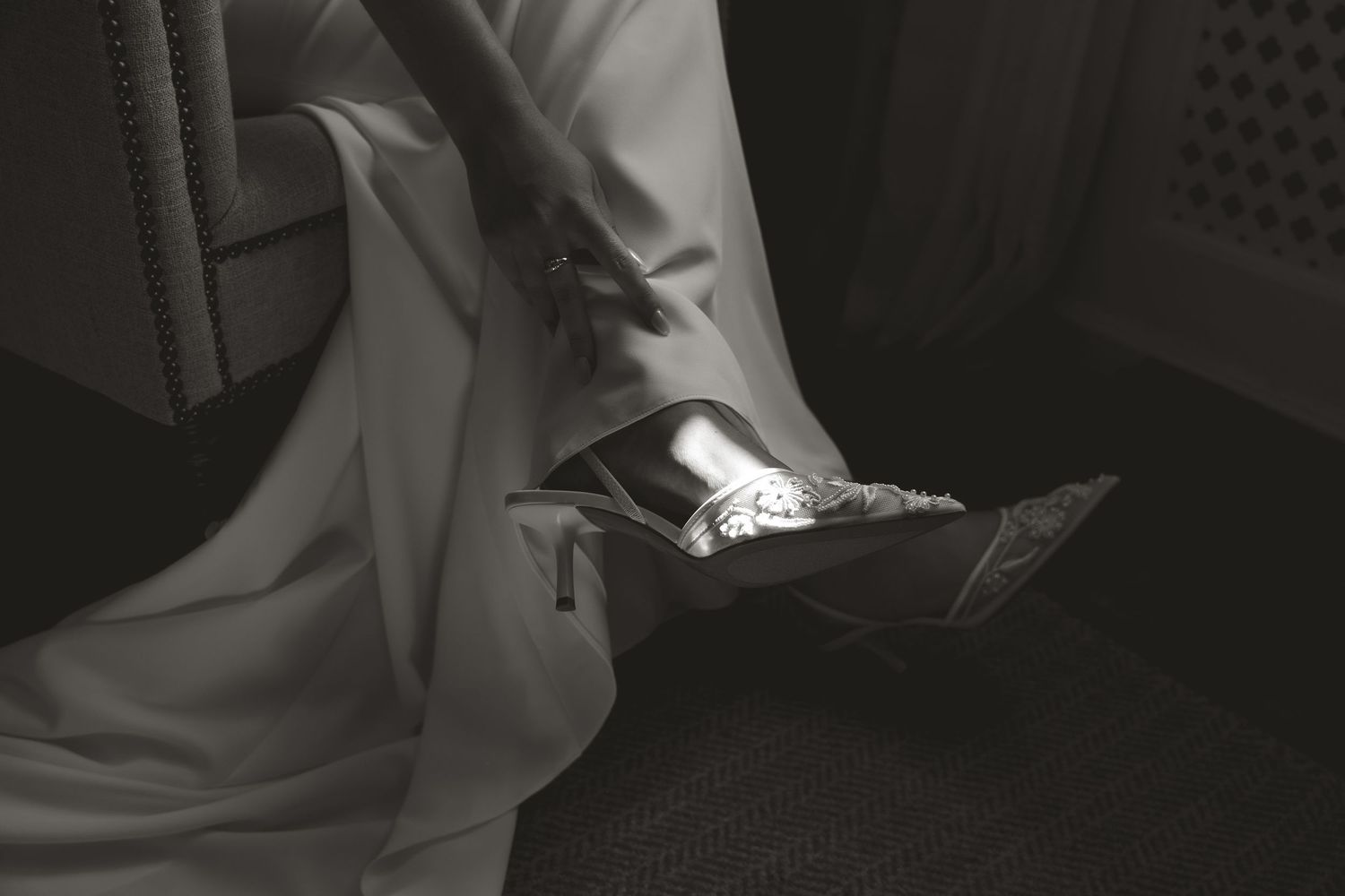Black and white photograph showing elegant formal shoes against dark fabric and clothing material.