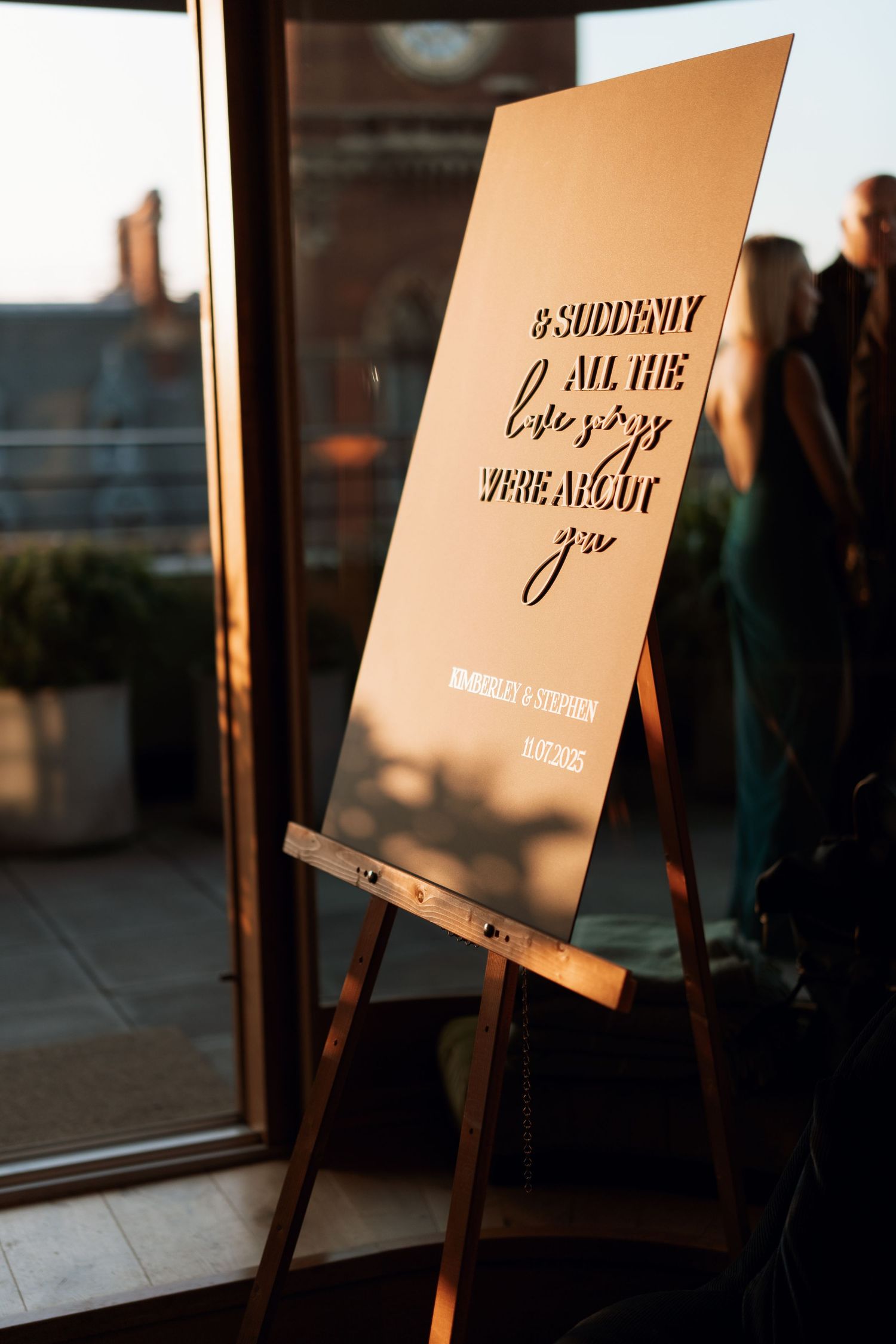 A wedding sign displayed on a wooden easel with calligraphy text at sunset.