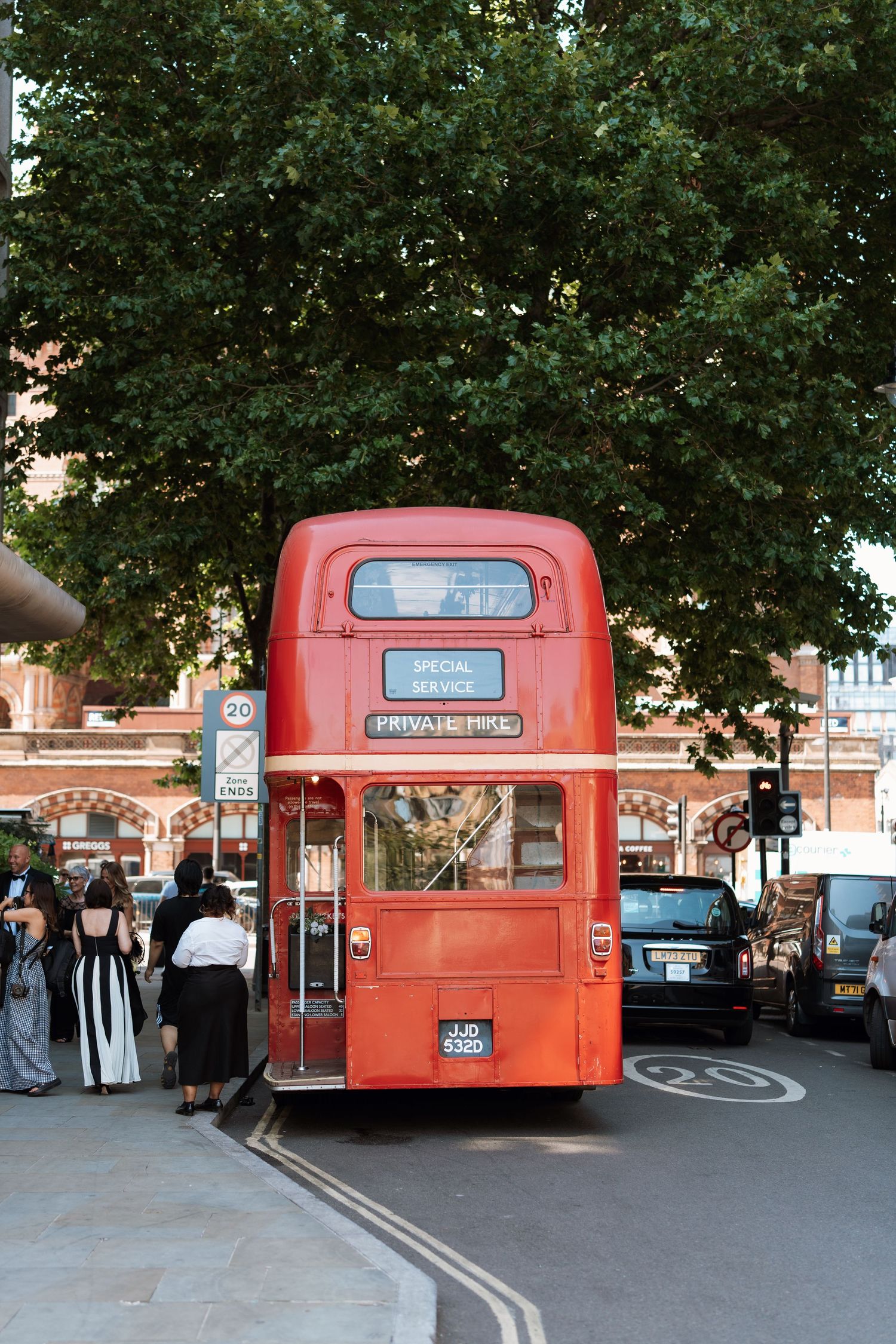 Vintage red double-decker bus parked on a London street with trees in the background.