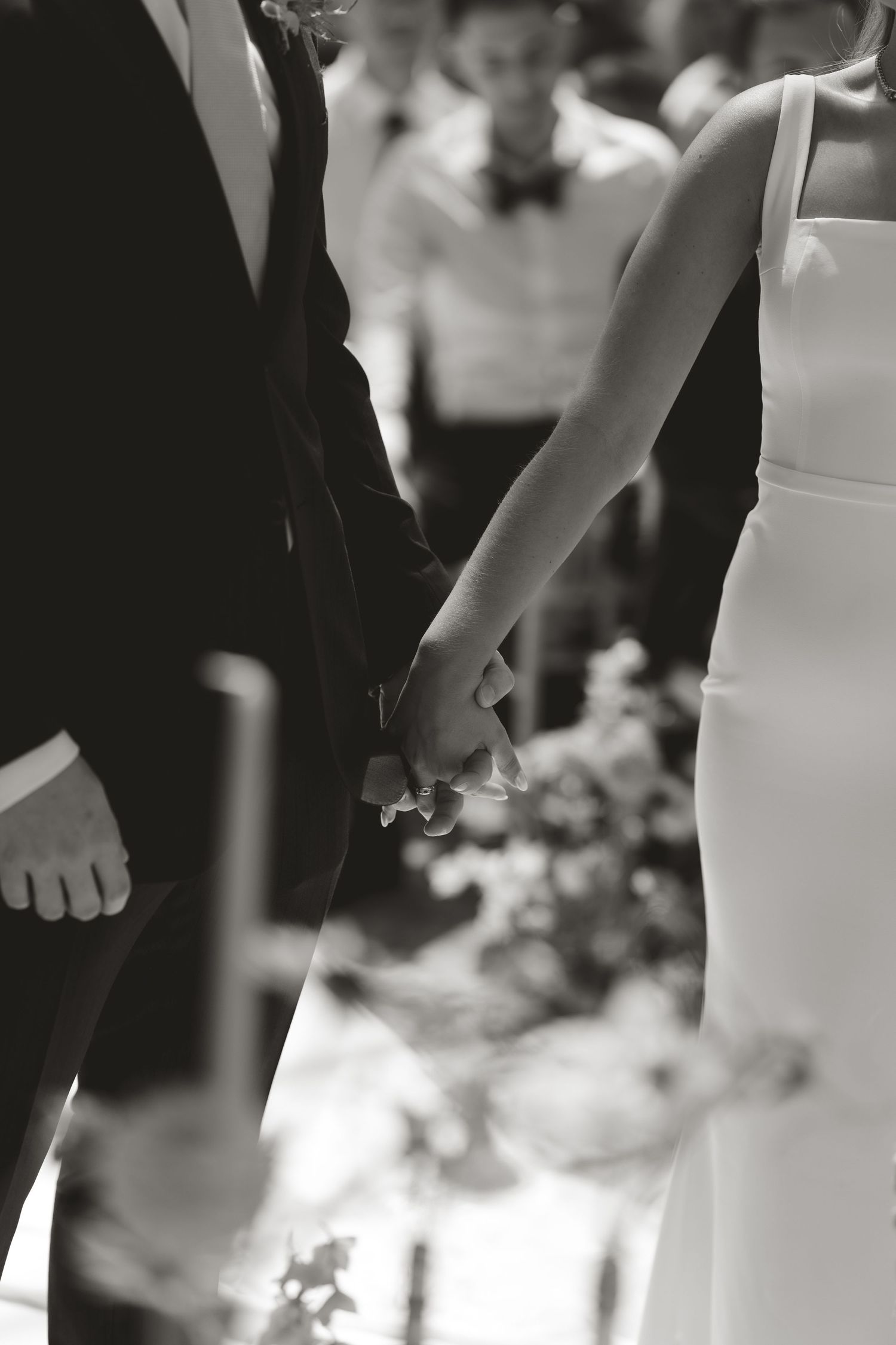A black and white close-up of a bride and groom holding hands at a wedding ceremony.