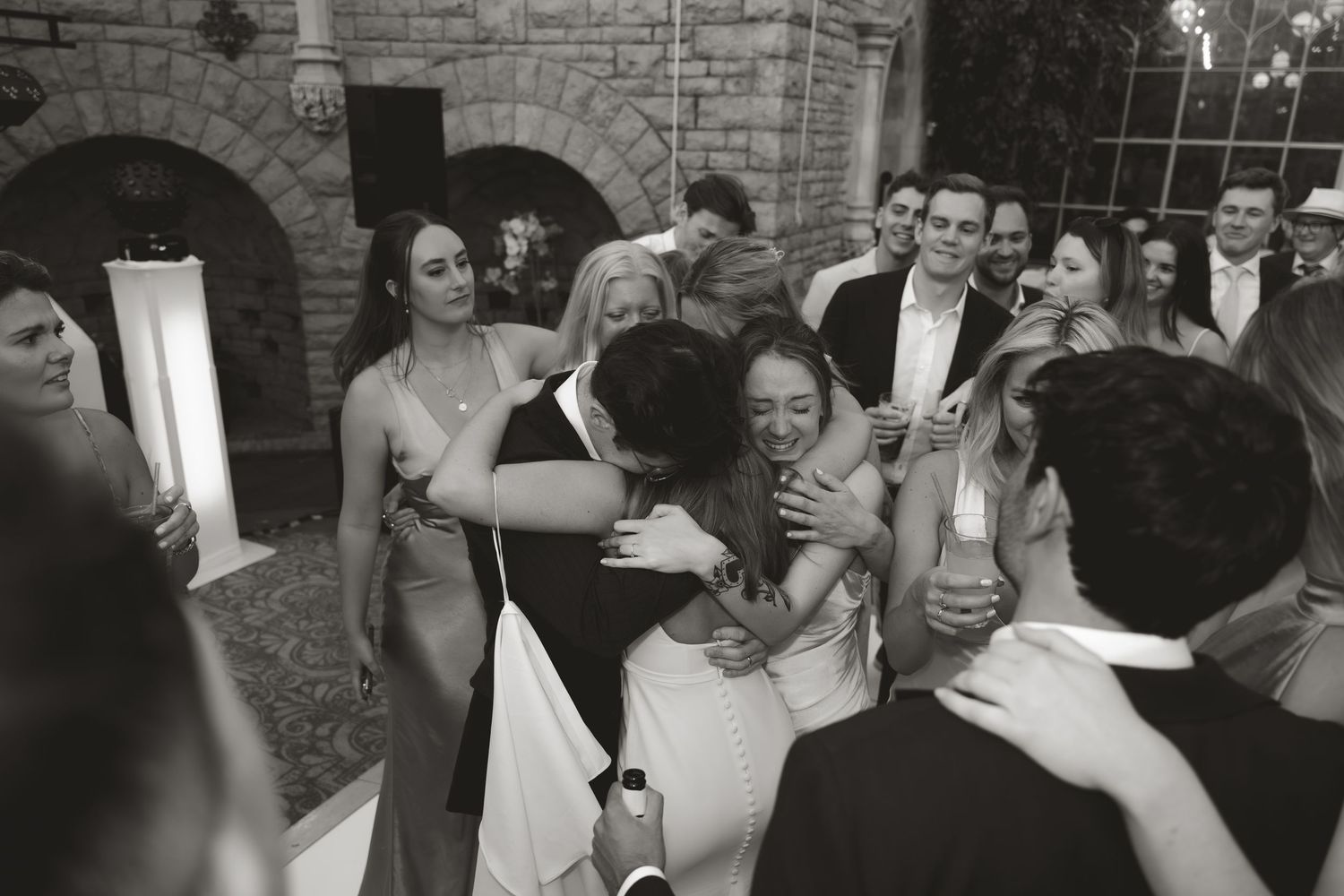 People embracing and celebrating at a joyous wedding reception inside a stone archway venue.
