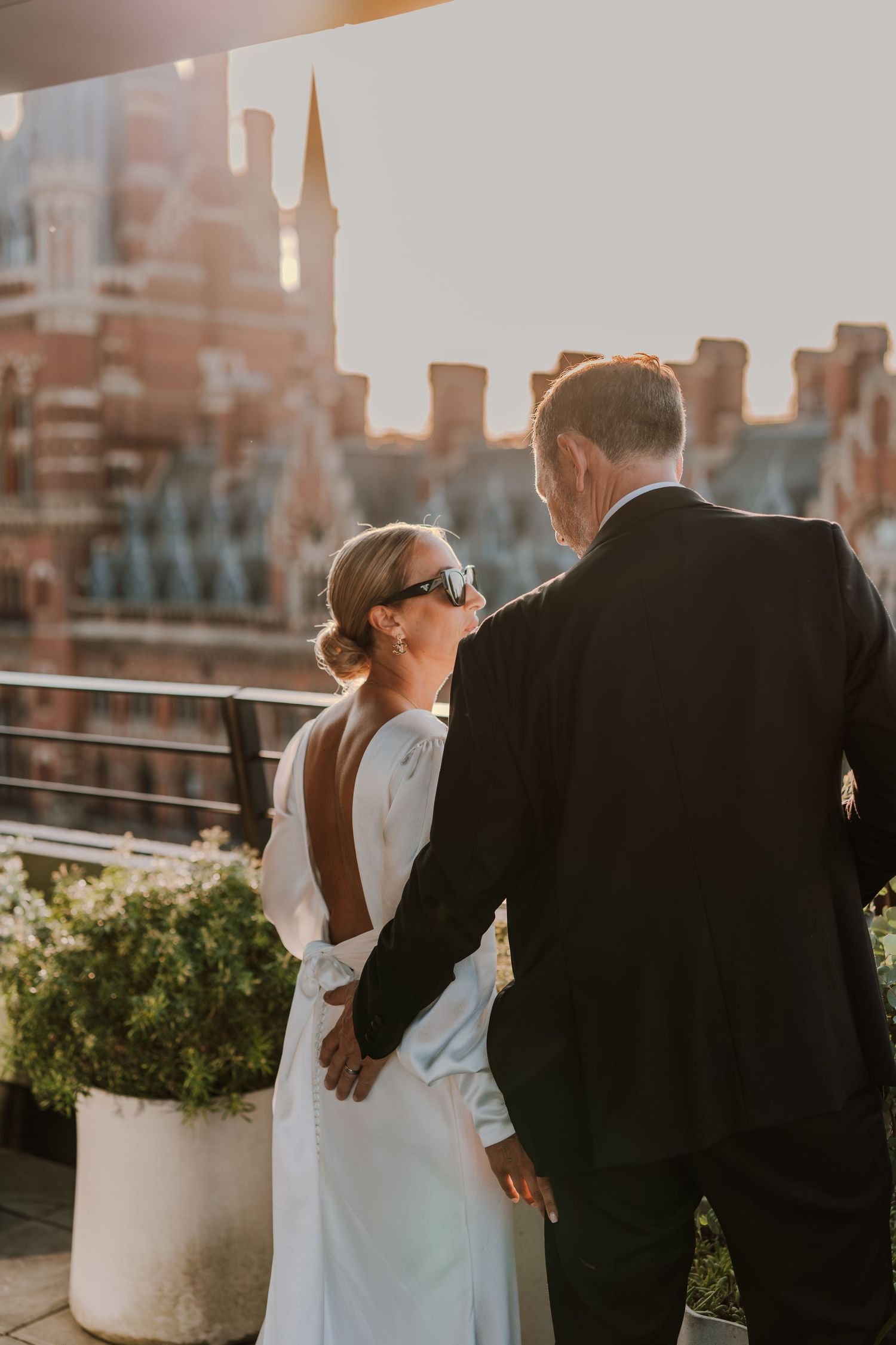 A couple in wedding attire sharing an intimate moment at sunset with urban architecture in the background.