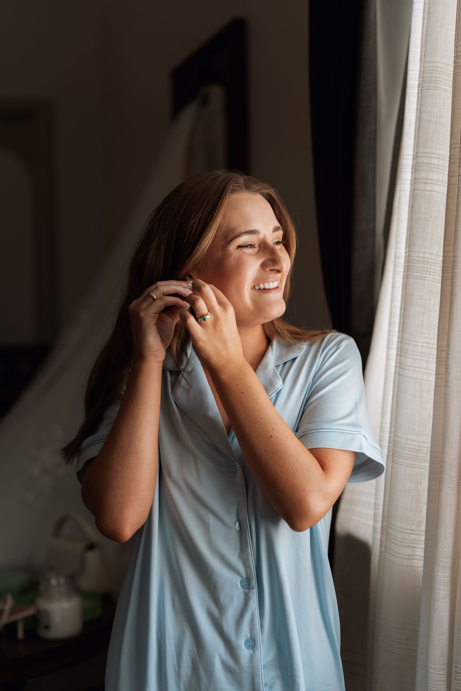 A person in a light blue shirt stands by a window and covers their ears while expressing discomfort.