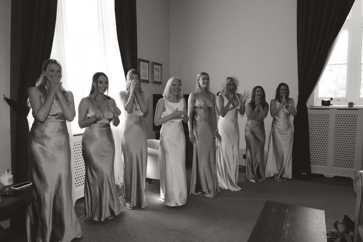 A group of bridesmaids wearing elegant silver gowns stand in a row in a formal black and white photograph.