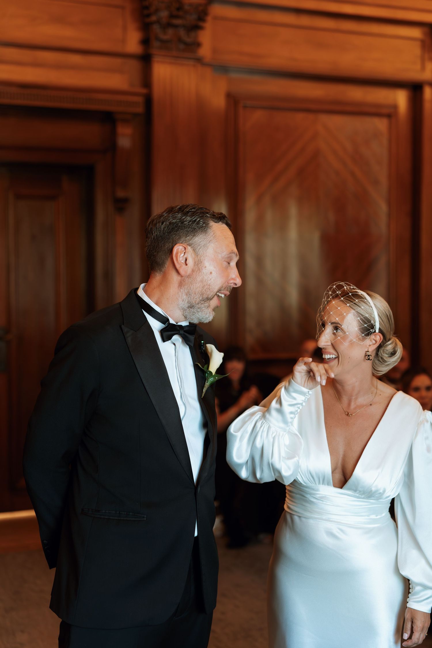 Elegant couple in formal wedding attire sharing a joyful moment together in a wood-paneled room.