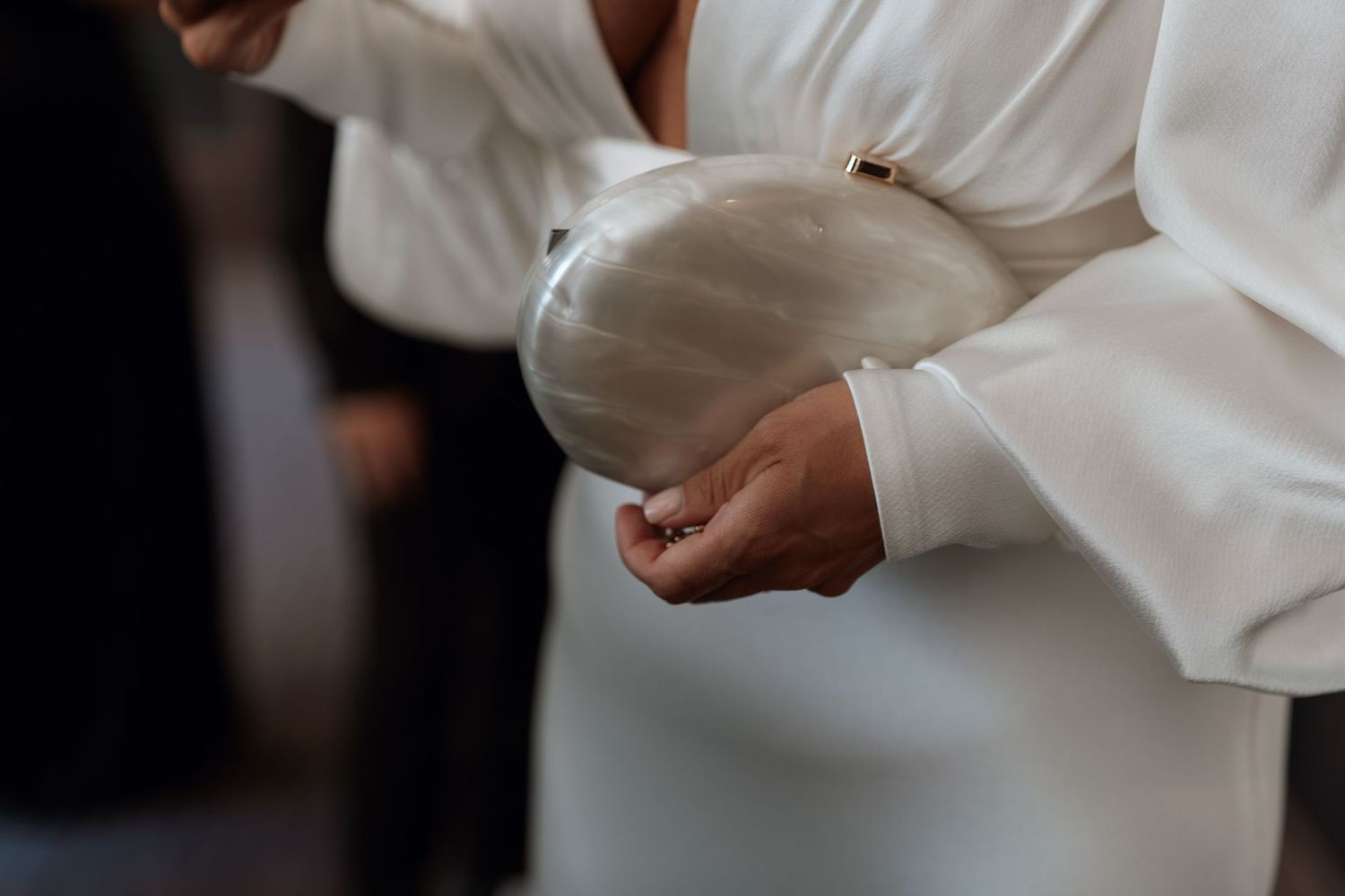 Close-up detail of hands adjusting a white silk dress or garment in soft lighting.