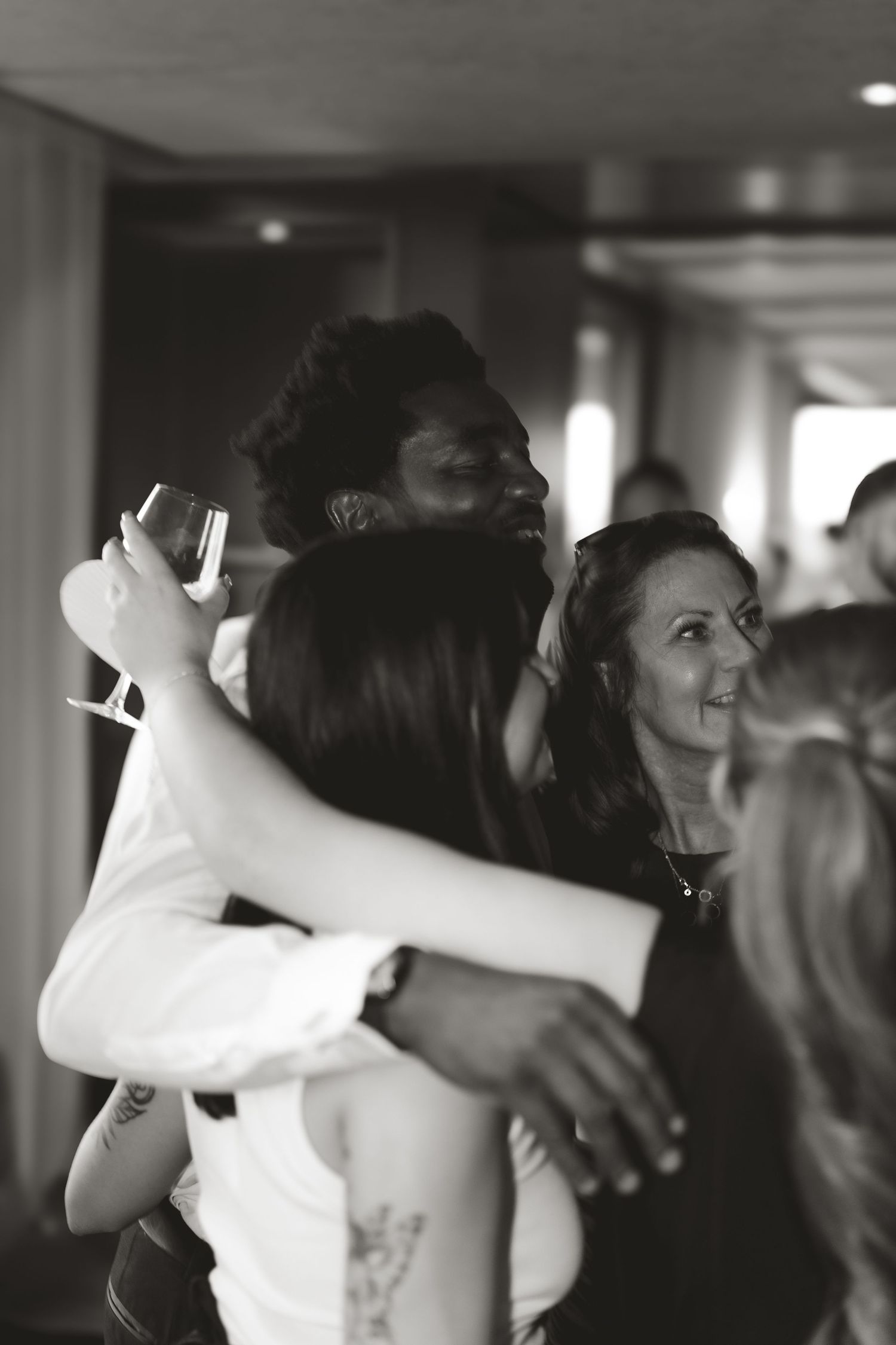 Black and white candid photo of wedding guests embracing during a reception celebration.