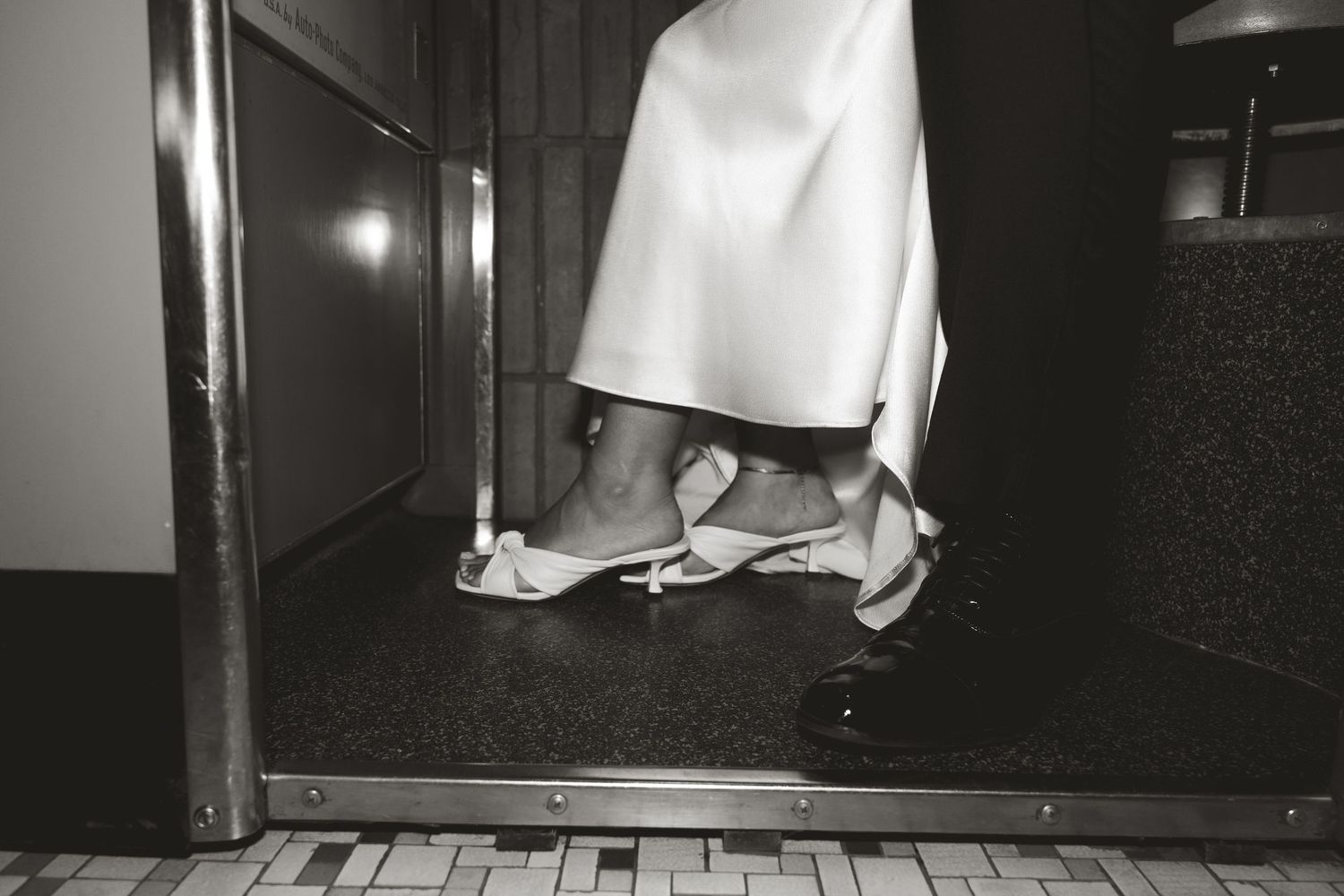 Black and white photo showing levitating white shoes and dress fabric floating above a wooden floor in a dark hallway.