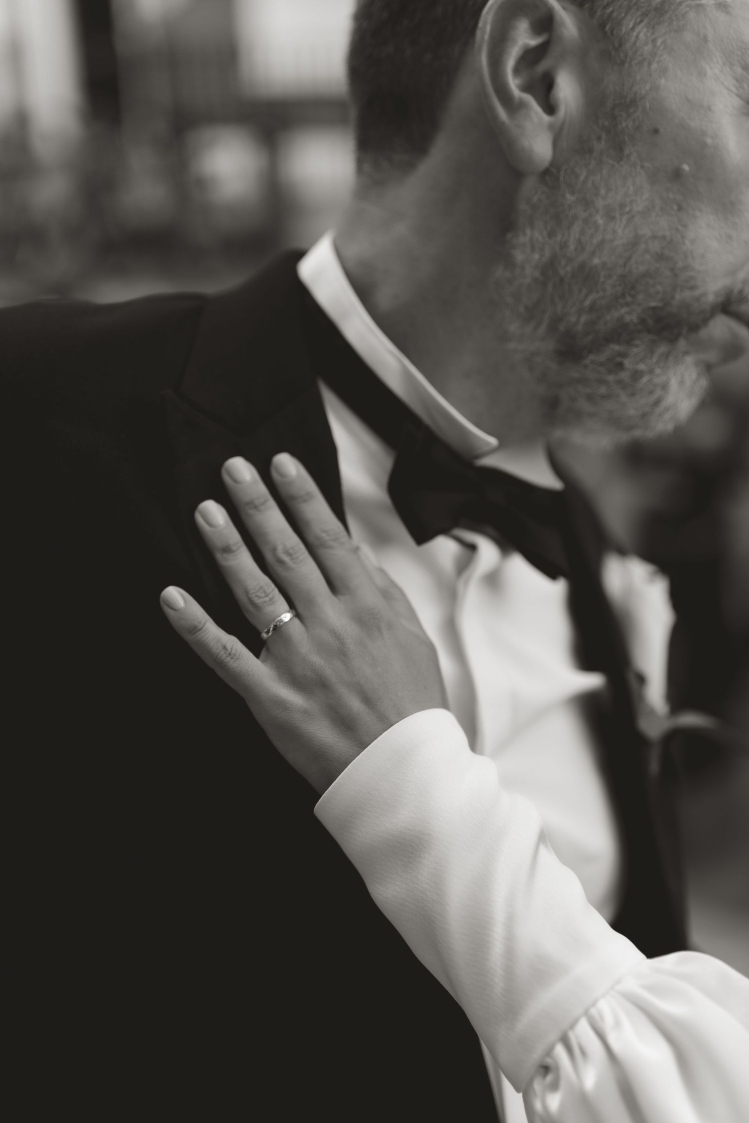 Close-up of couple embracing, showing wedding ring and formal attire details.