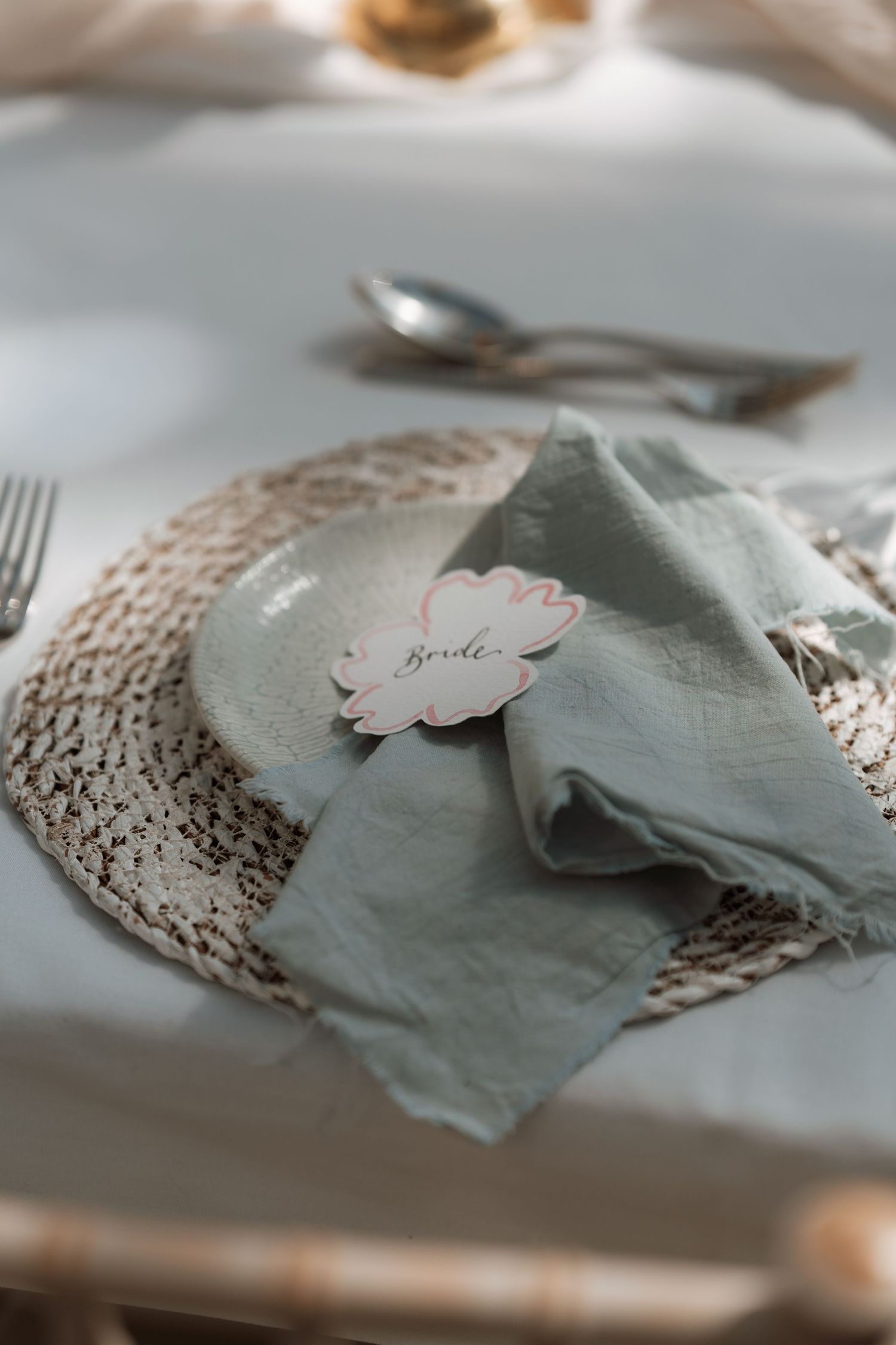Elegant table setting with sage green napkin and name card on delicate lace placemat with silverware.