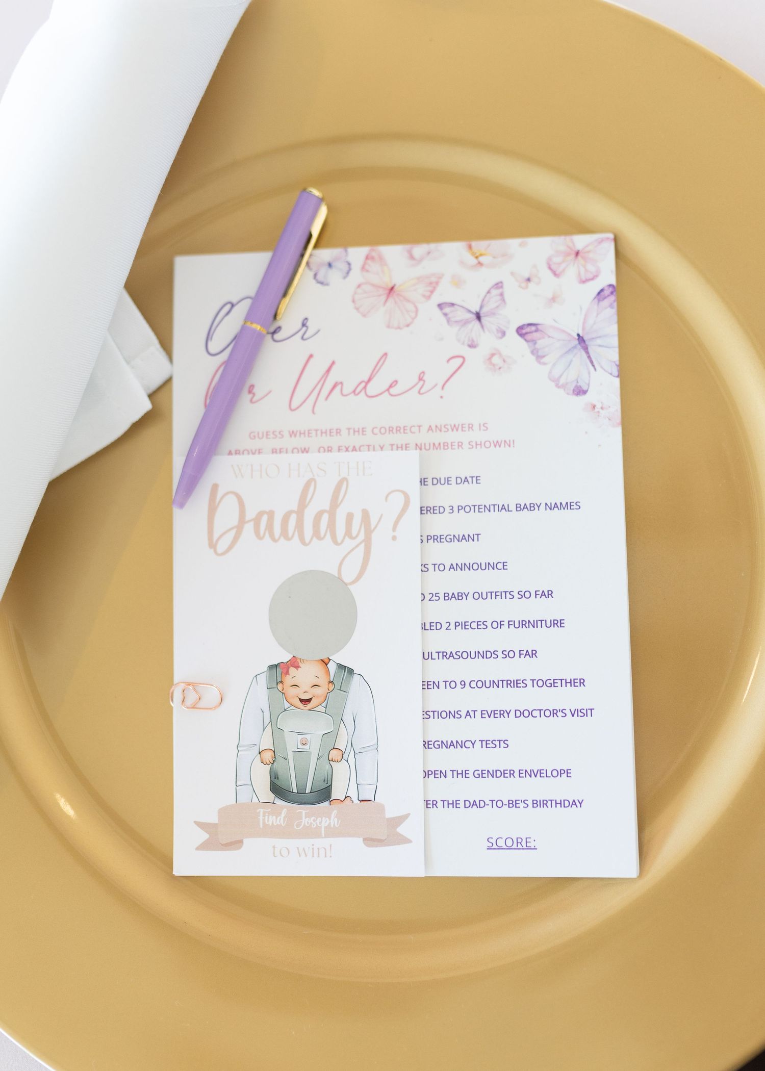 Over or Under daddy-themed baby shower game card with purple pen on a gold charger plate.