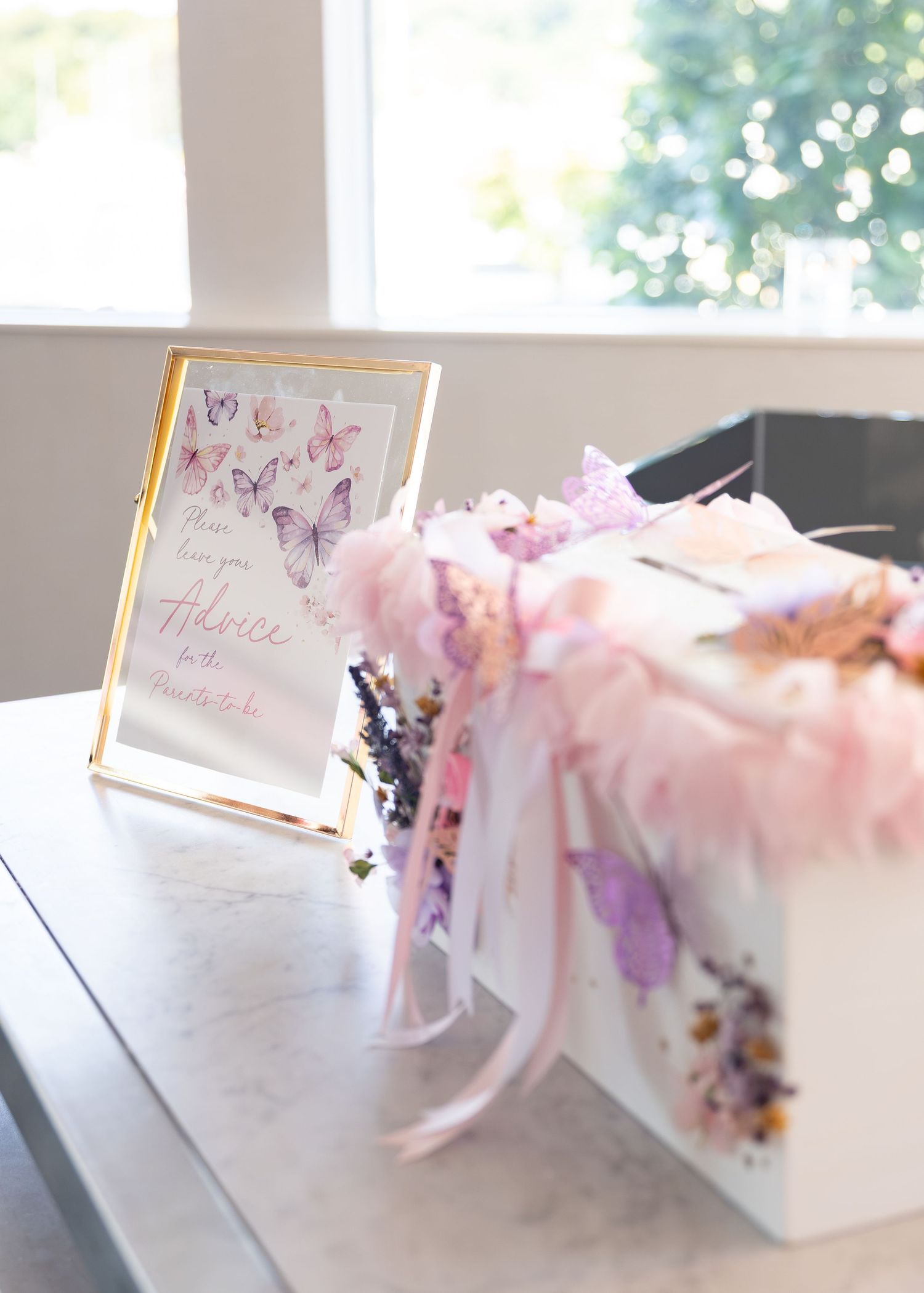 Gold-framed advice for mommy-to-be sign with butterfly decor next to a white gift box at a baby shower.