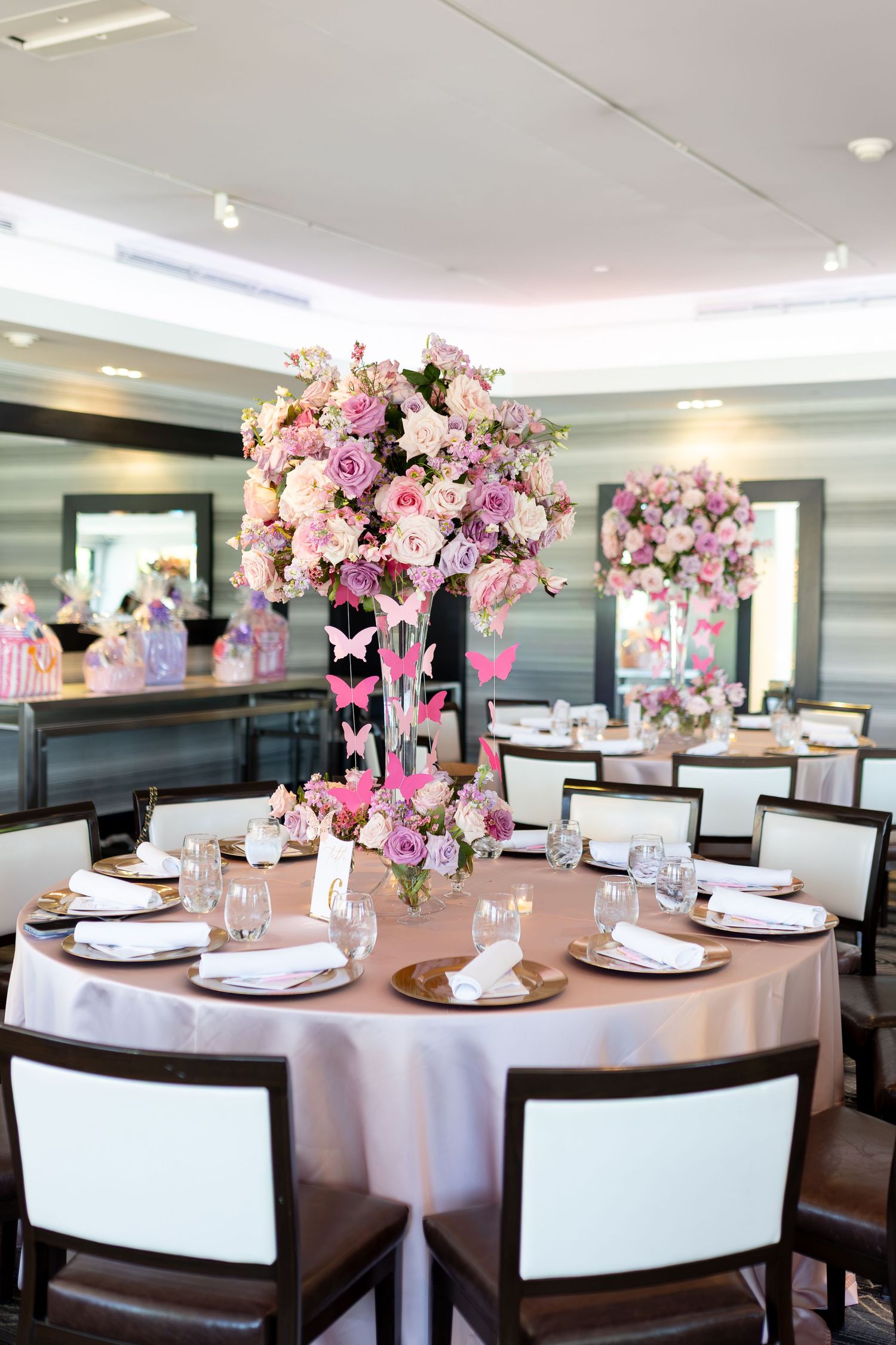 Elegant baby shower table with tall pink floral centerpiece, butterfly accents, gold chargers, and pink tablecloth.