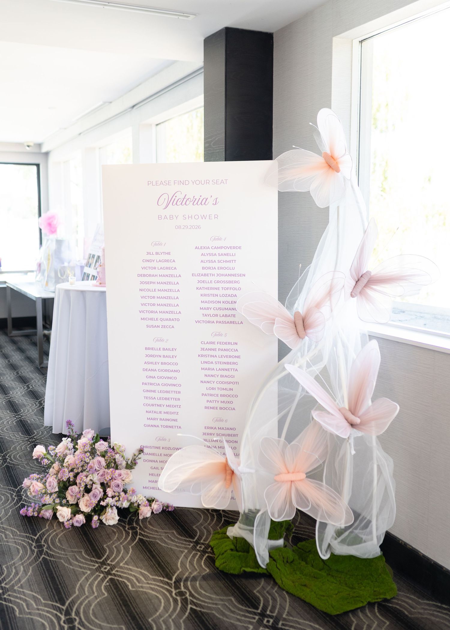 Elegant baby shower seating chart display decorated with pink floral arrangements and butterfly tulle accents.