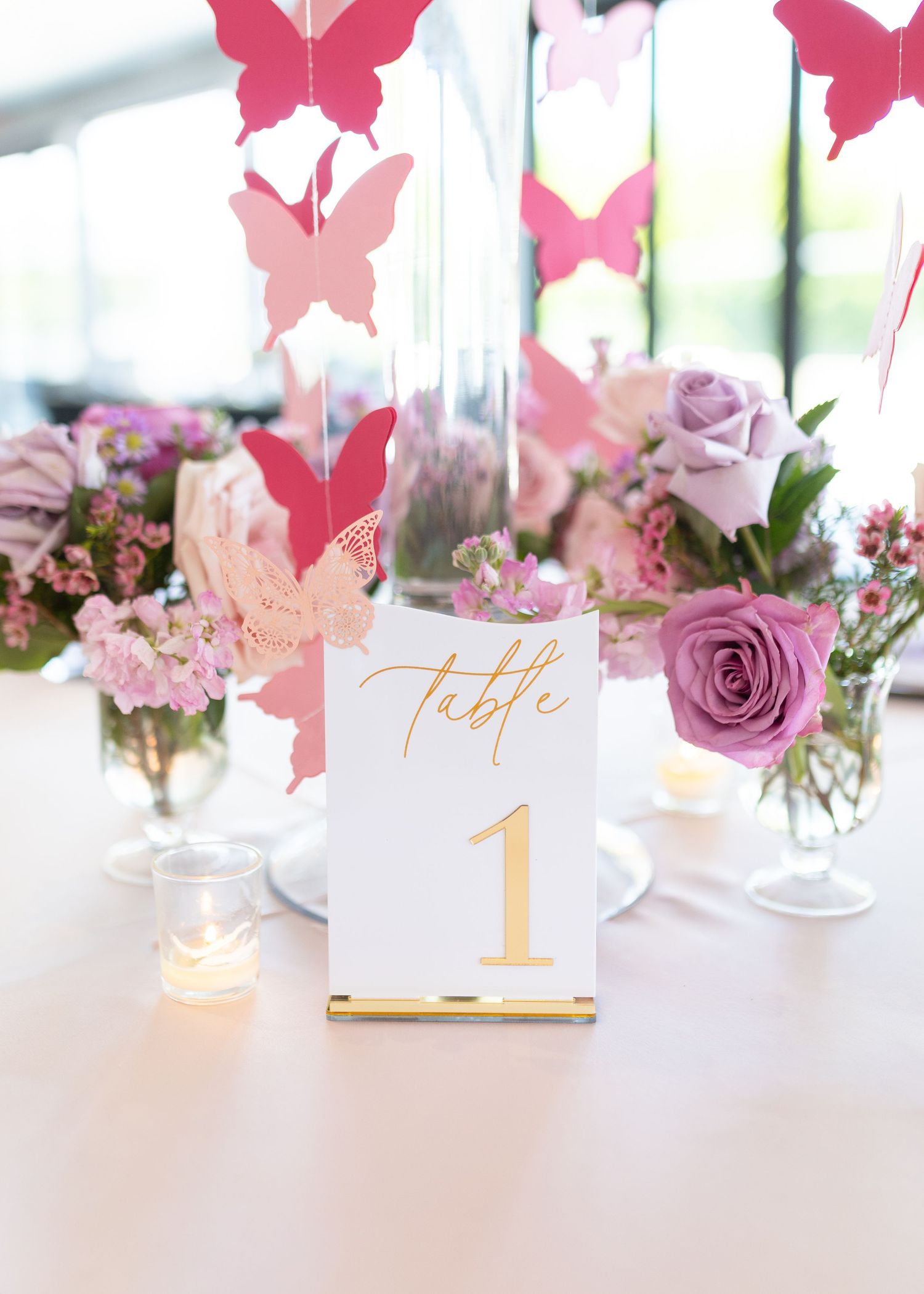 Baby shower table centerpiece featuring butterfly garlands, purple roses, and a gold Table 1 number card.