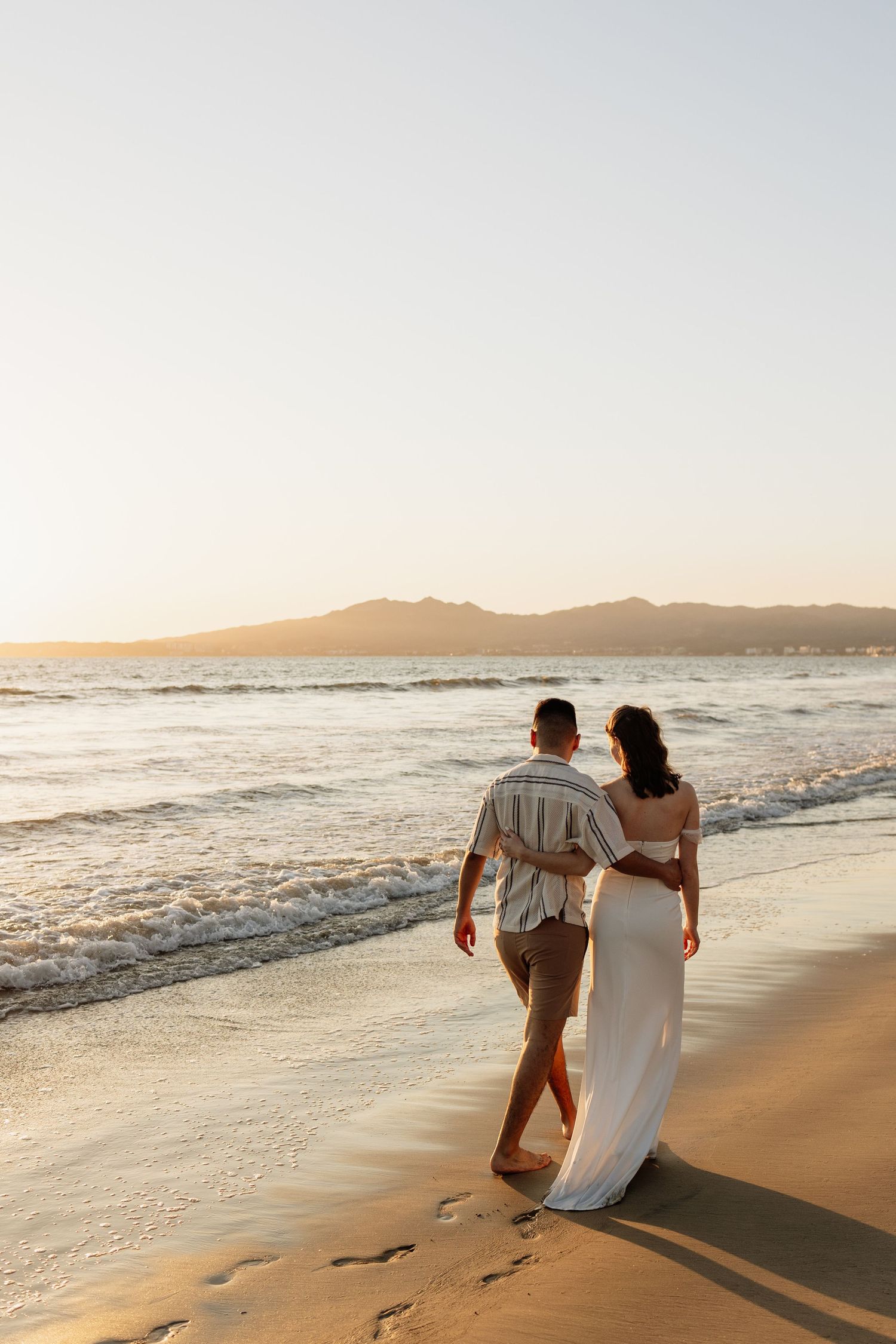 Parents-to-be walking hand-in-hand on Punta Mita beach during golden hour
